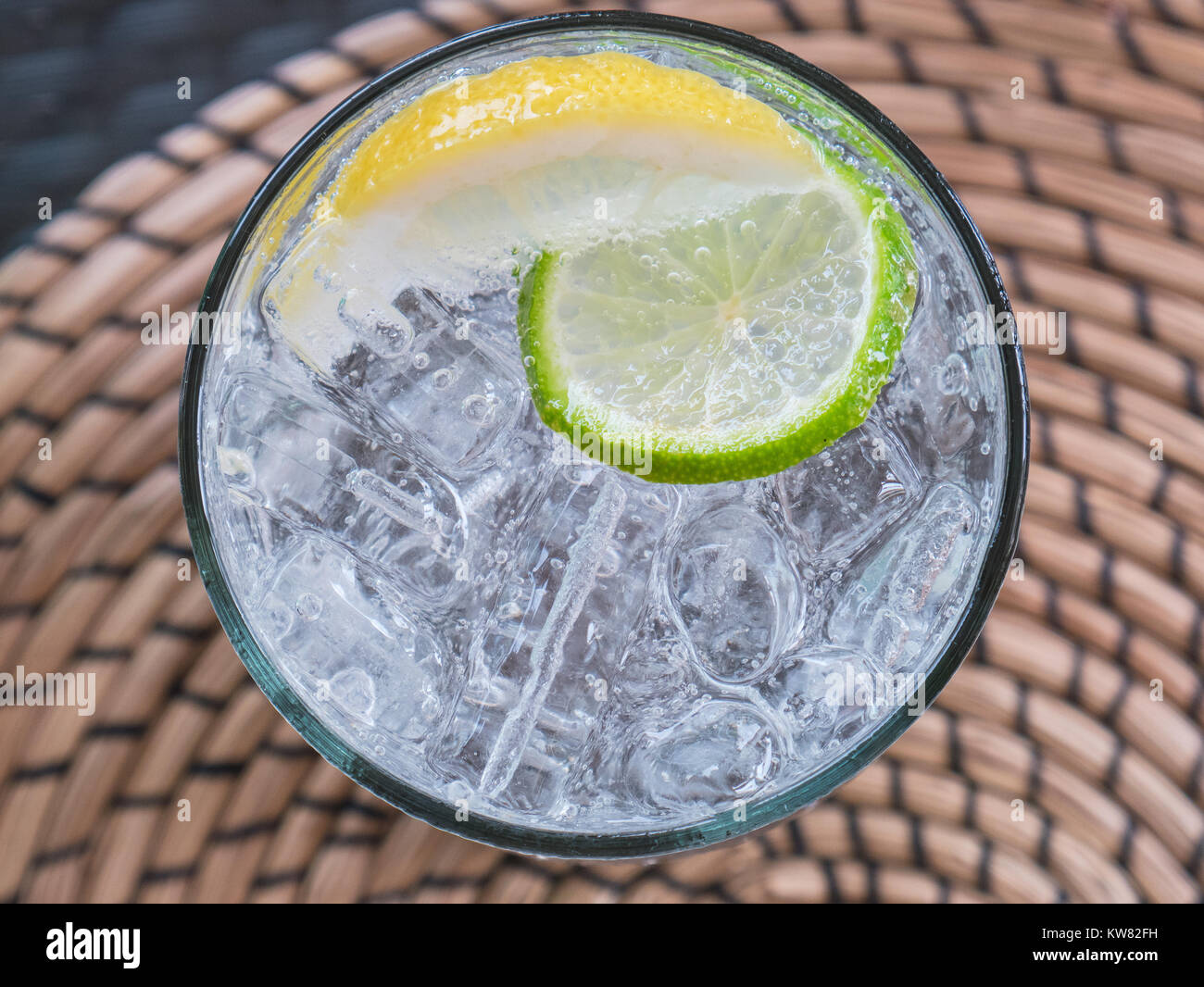 Bicchiere di acqua di soda con ghiaccio a cubetti, una fetta di limone e una fettina di limone. Il vetro è direttamente visibile dal di sopra, in piedi su un round placemat. Solo th Foto Stock