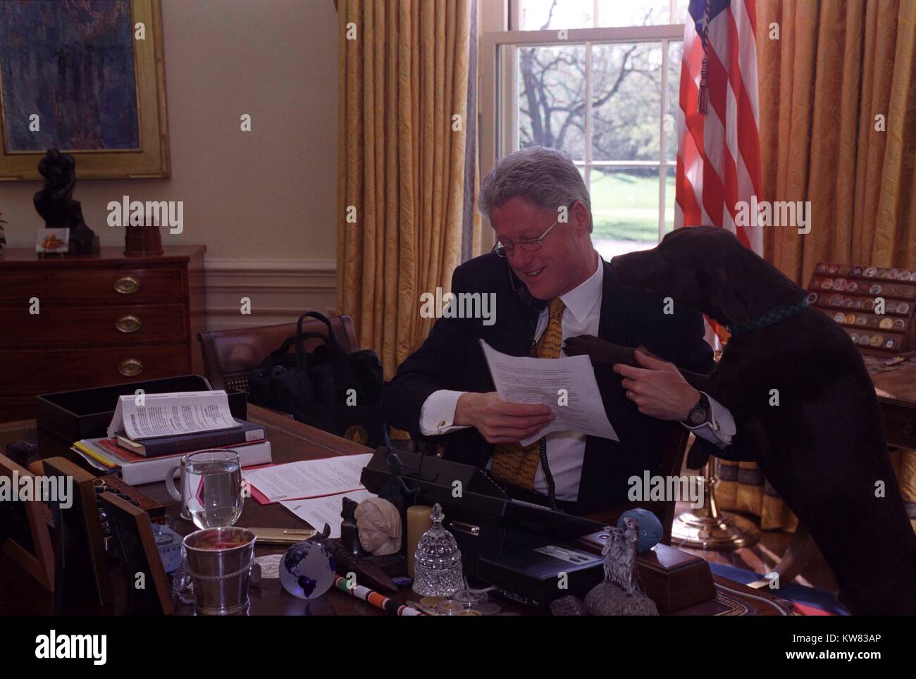 Il presidente William Jefferson Clinton seduto alla sua scrivania e al telefono con il Presidente russo Boris Eltsin, Buddy il cane appoggiato la testa sulla spalla, Aprile 4, 1998. Foto Stock