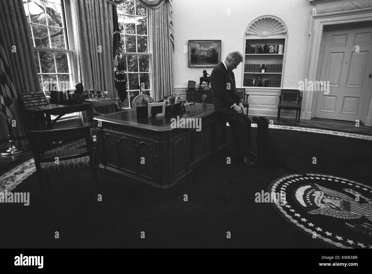 Dentro il suo ufficio ovale, il presidente Bill Clinton si appoggia contro la sua scrivania con le sue mani nel suo giro, guardando verso il basso in un primo momento il Pet, Buddy il cane, un marrone moca labrador, che siede diligentemente con lo sguardo rivolto verso il suo proprietario, all'interno della Casa Bianca di Washington, Distretto di Columbia, 16 gennaio 1998. Foto Stock