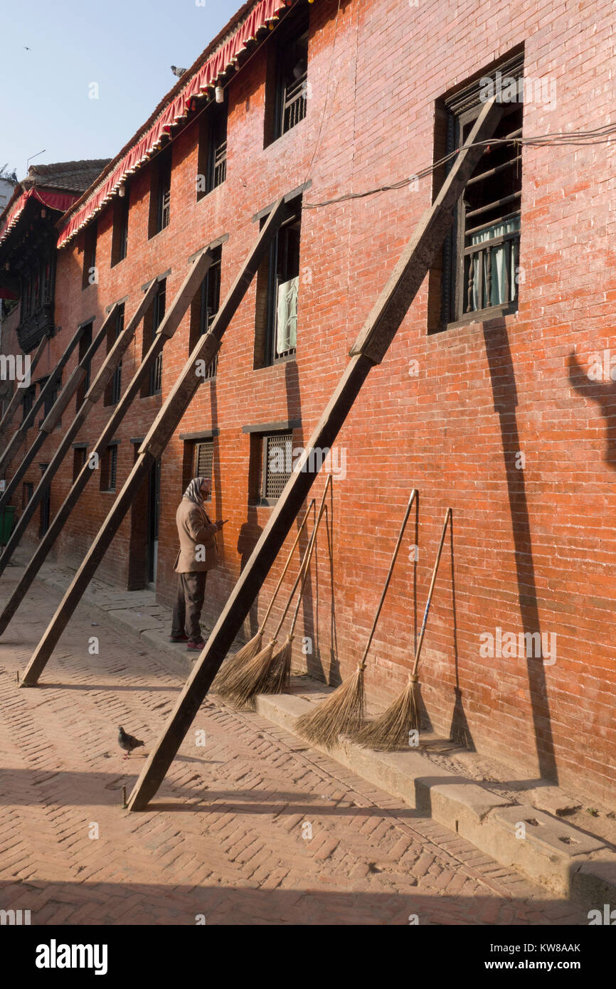 L'uomo sul cellulare sorge accanto al terremoto edificio danneggiato puntellato con supporti in legno a Kathmandu in Nepal Foto Stock