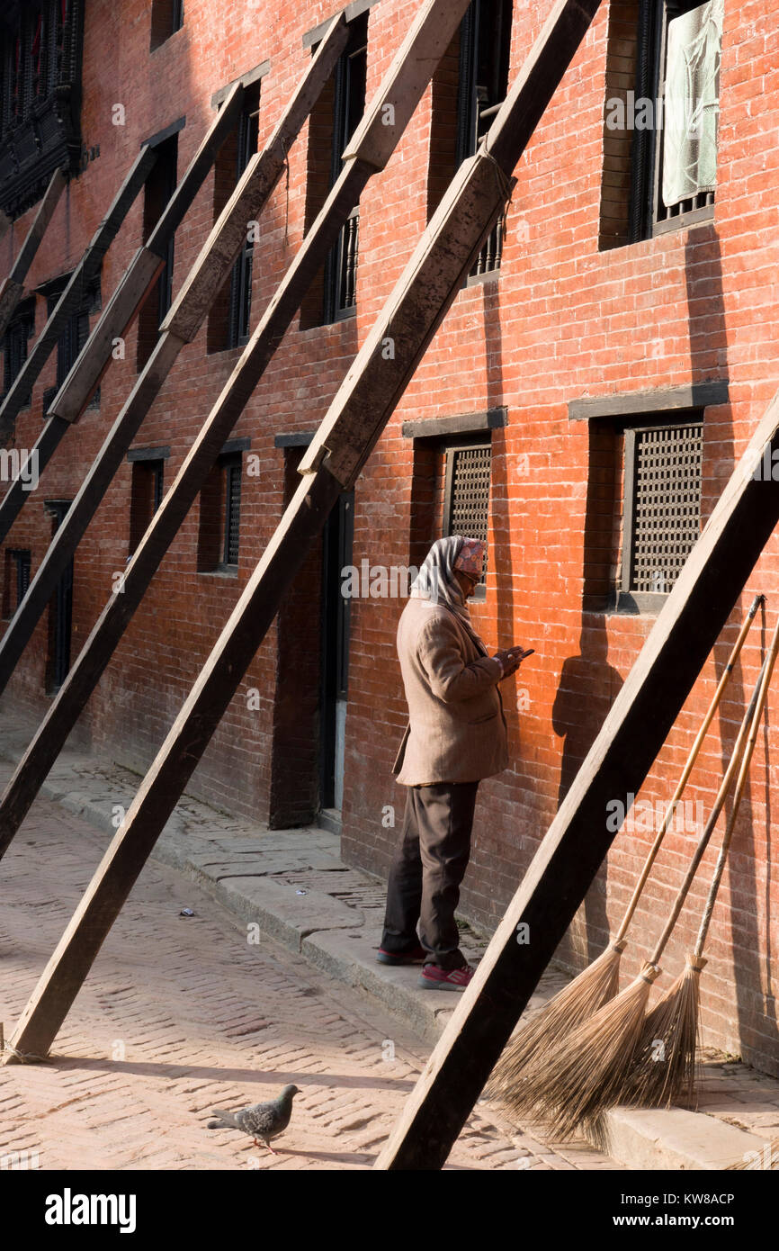 L'uomo sul cellulare sorge accanto al terremoto edificio danneggiato puntellato con supporti in legno a Kathmandu in Nepal Foto Stock