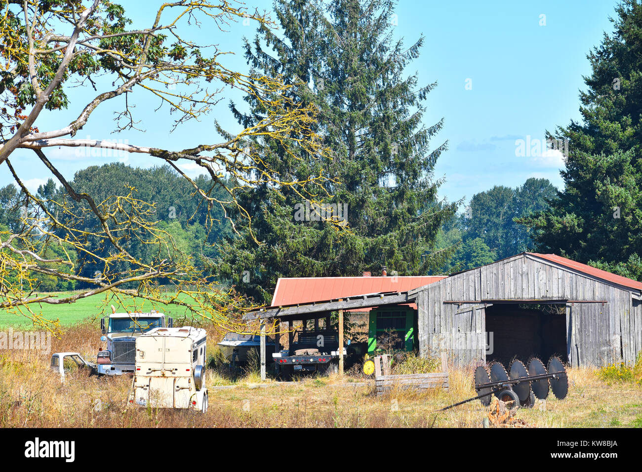 Un vecchio fienile spiovente con attrezzature agricole, barca, autocarro a pianale e rimorchio cavallo nel nord-ovest del pacifico paesaggio della città di Bellingha Foto Stock