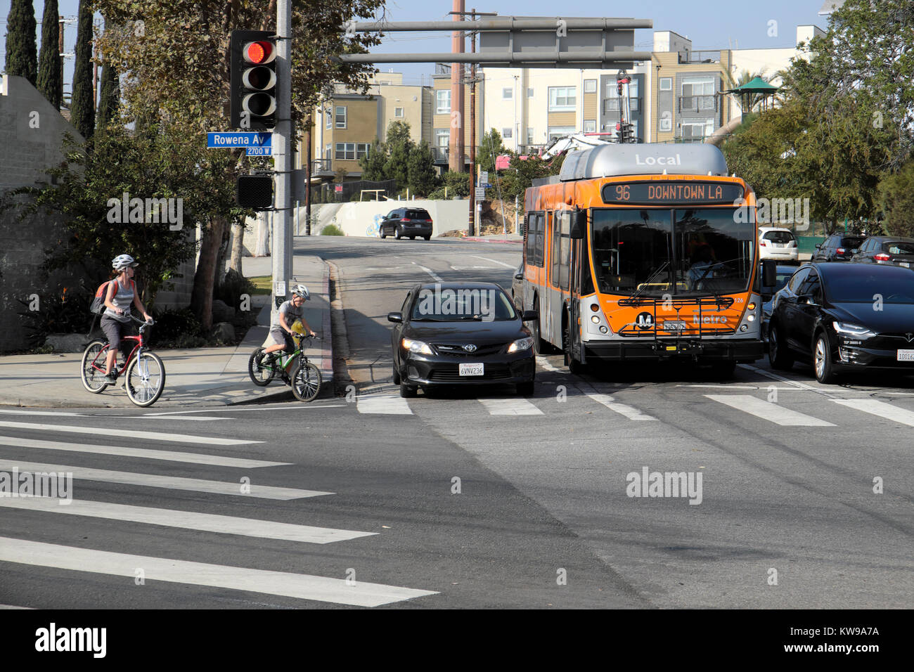 La madre e il bambino su moto di attendere per il traffico e il bus per attraversare la strada al semaforo su Rowena Ave Silver Lake, Los Angeles, California, KATHY DEWITT Foto Stock