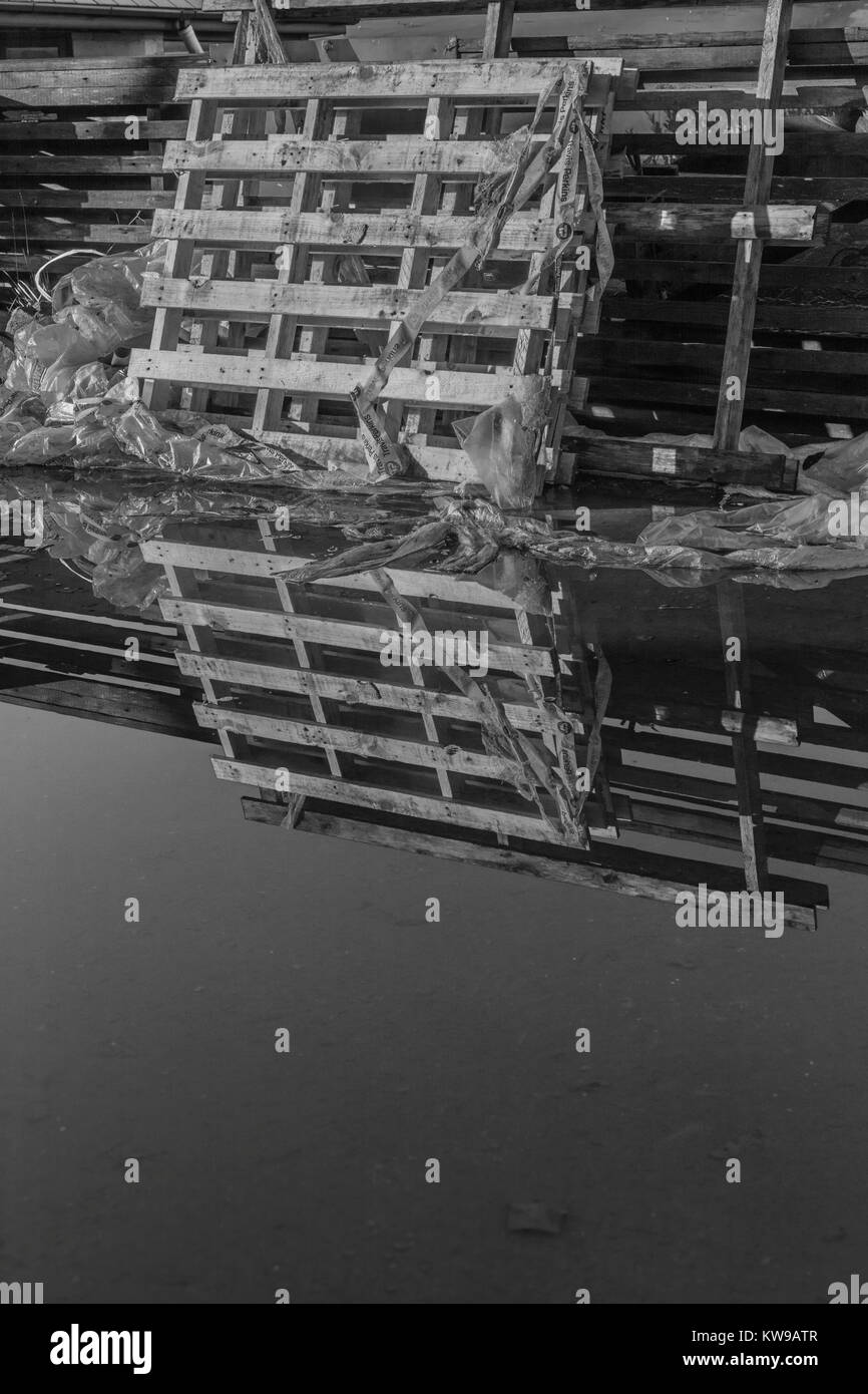 Black & White immagine dell edificio fornisce pallet riflessa in acqua a un piccolo sito in costruzione - metafora per flessione nel settore delle costruzioni. Foto Stock