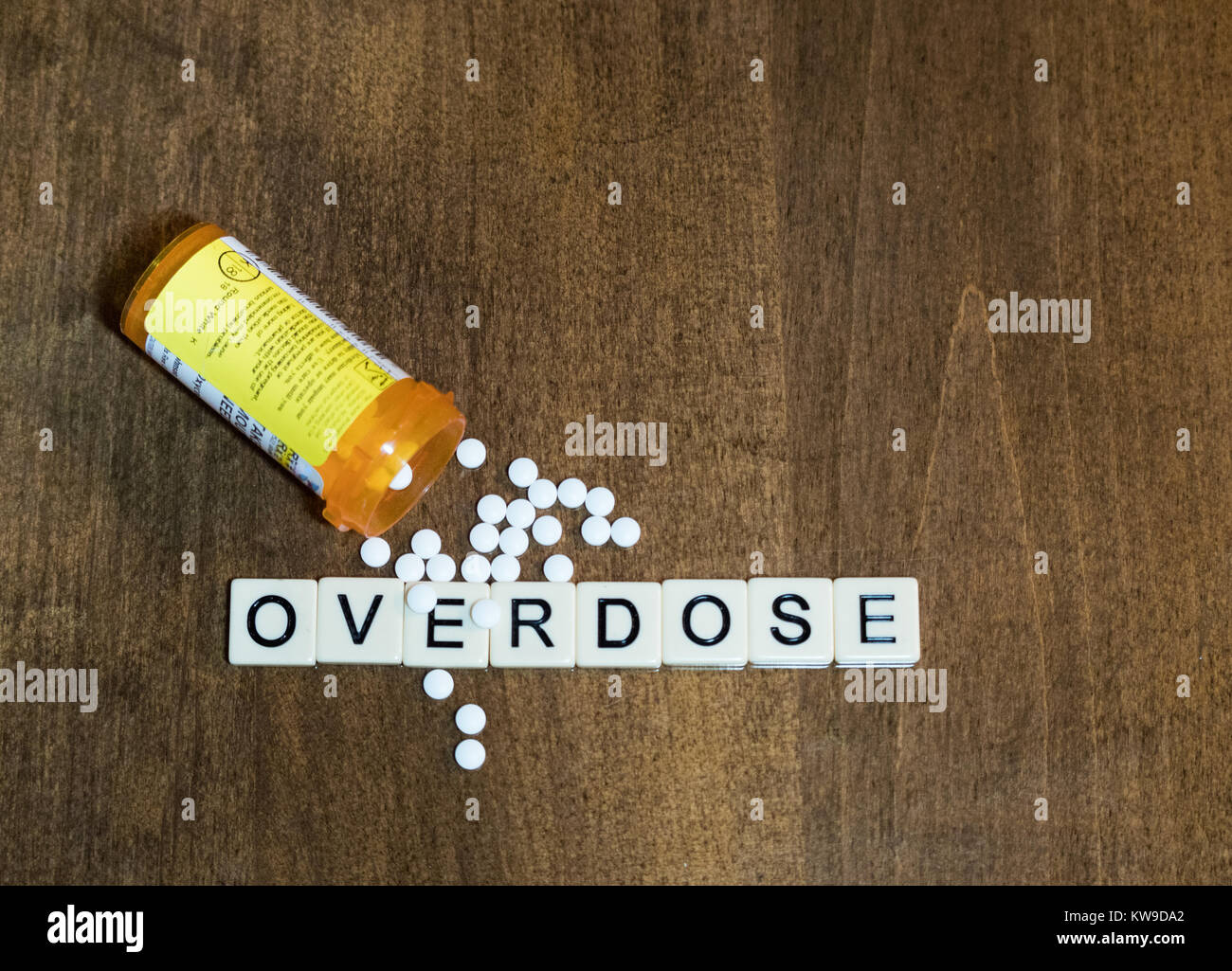 Overdose scritto con lettere di piastrella in una fila con piccole pillole di bianco e una prescrizione di aprire la bottiglia. Fotografato dal di sopra su un tavolo di legno. Foto Stock