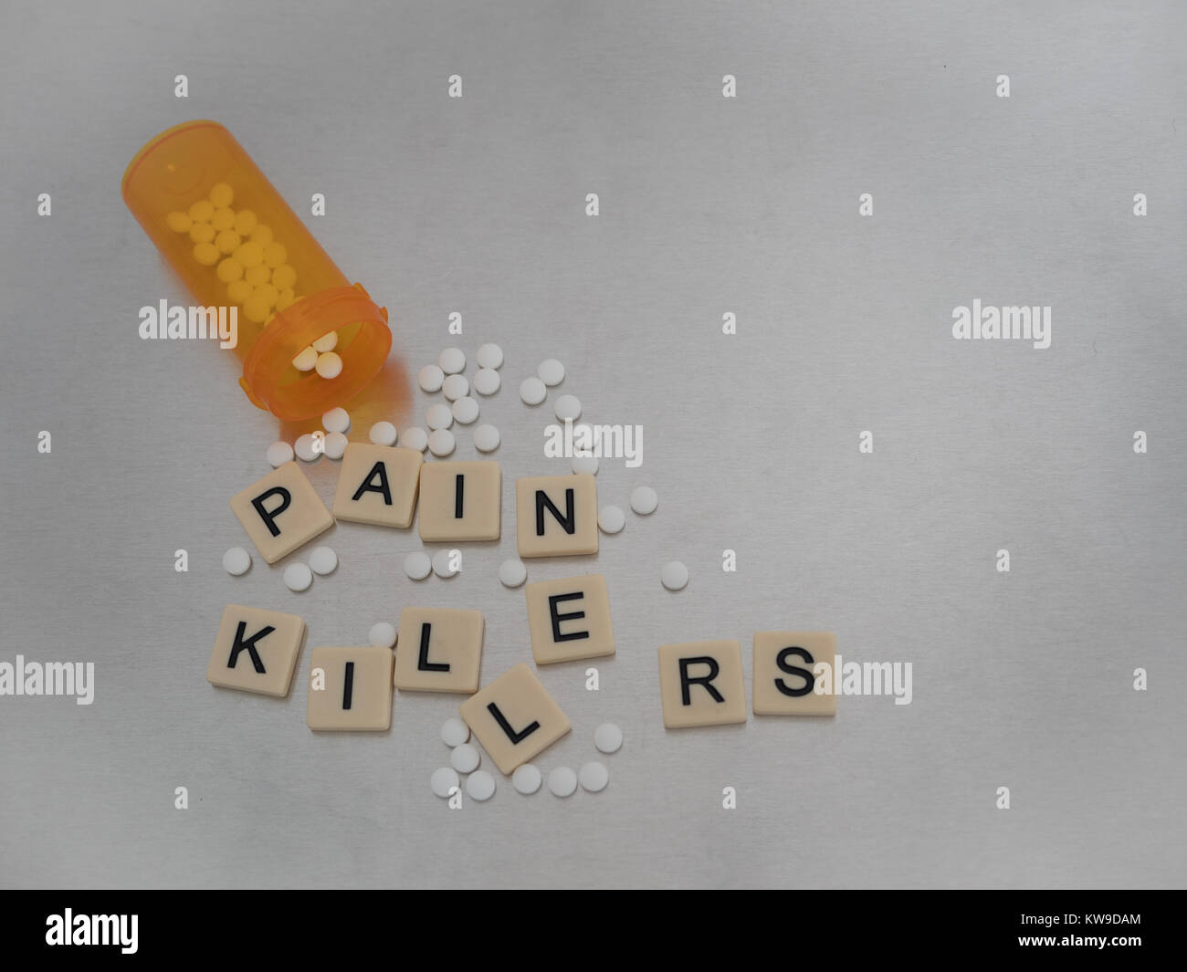 Pain Killer scritto con lettere di piastrelle collocato in modo casuale con una bottiglia aperta di pastiglie di ossicodone. Fotografato dal di sopra in acciaio inossidabile Foto Stock