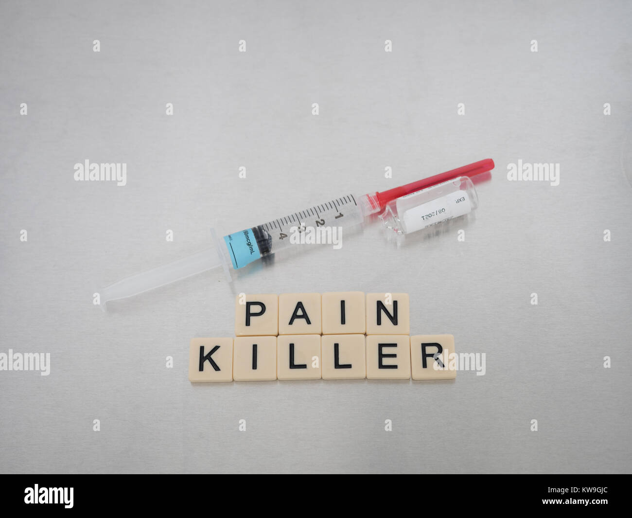 Pain Killer scritto con lettere di piastrelle collocato in una riga con una siringa riempita con liquido chiaro e un bicchiere vuoto fentanil flaconcino sul suo lato. Foto Stock