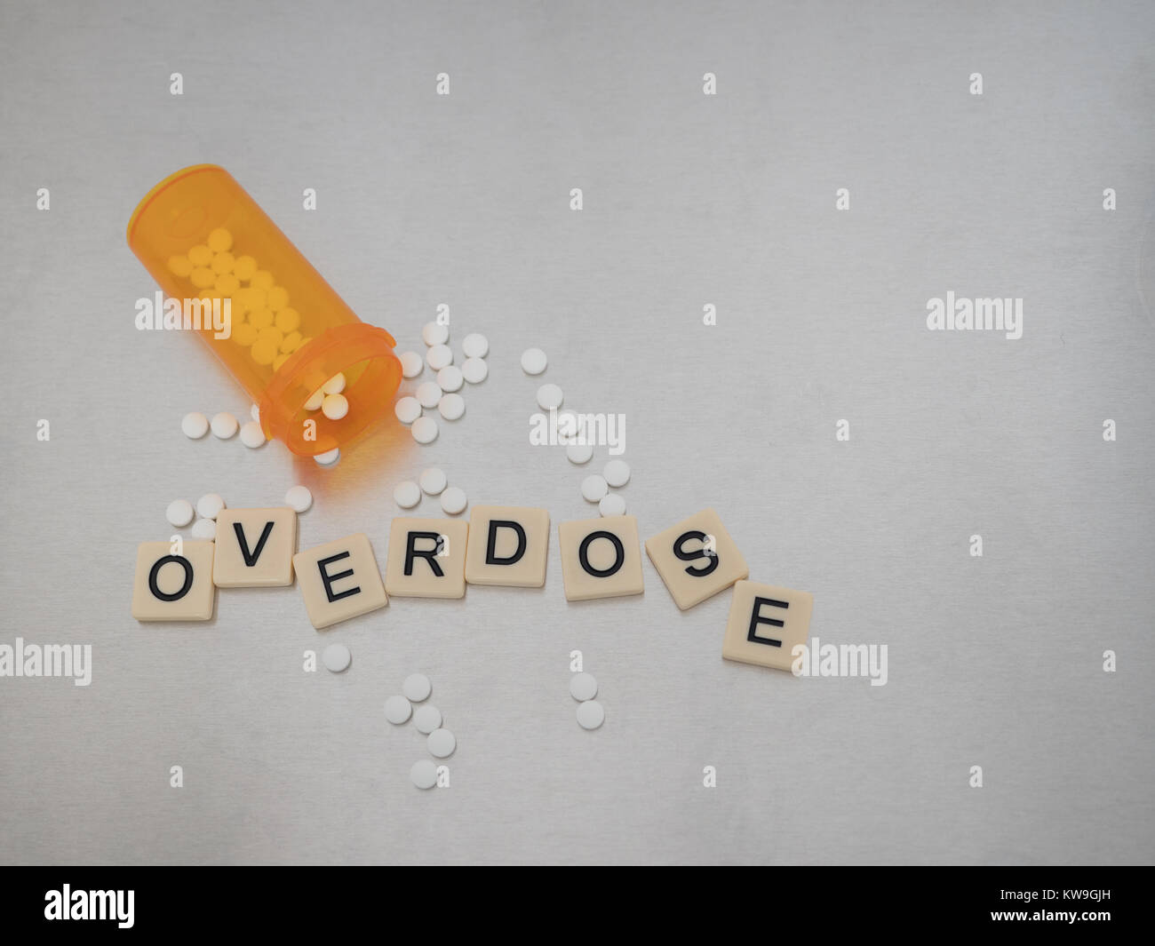 Overdose scritto con lettere di piastrelle collocato in un casuale con una bottiglia aperta di pastiglie di ossicodone. Fotografato dal di sopra su acciaio inossidabile. Foto Stock