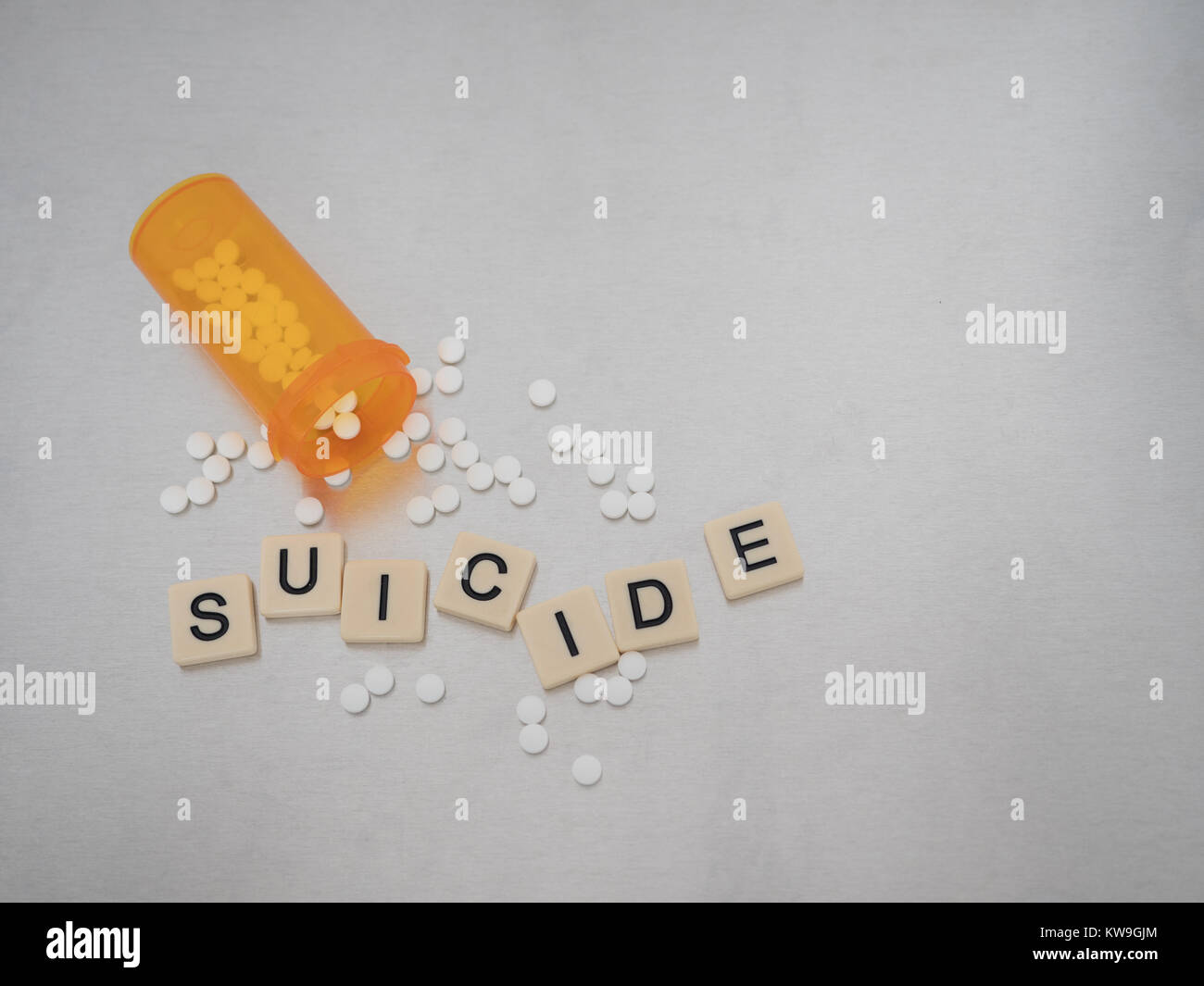 "Suicide' scritto con lettere di piastrelle collocato in un casuale con la bottiglia aperta di ossicodone pillole. Fotografato dal di sopra su un acciaio inossidabile. Foto Stock