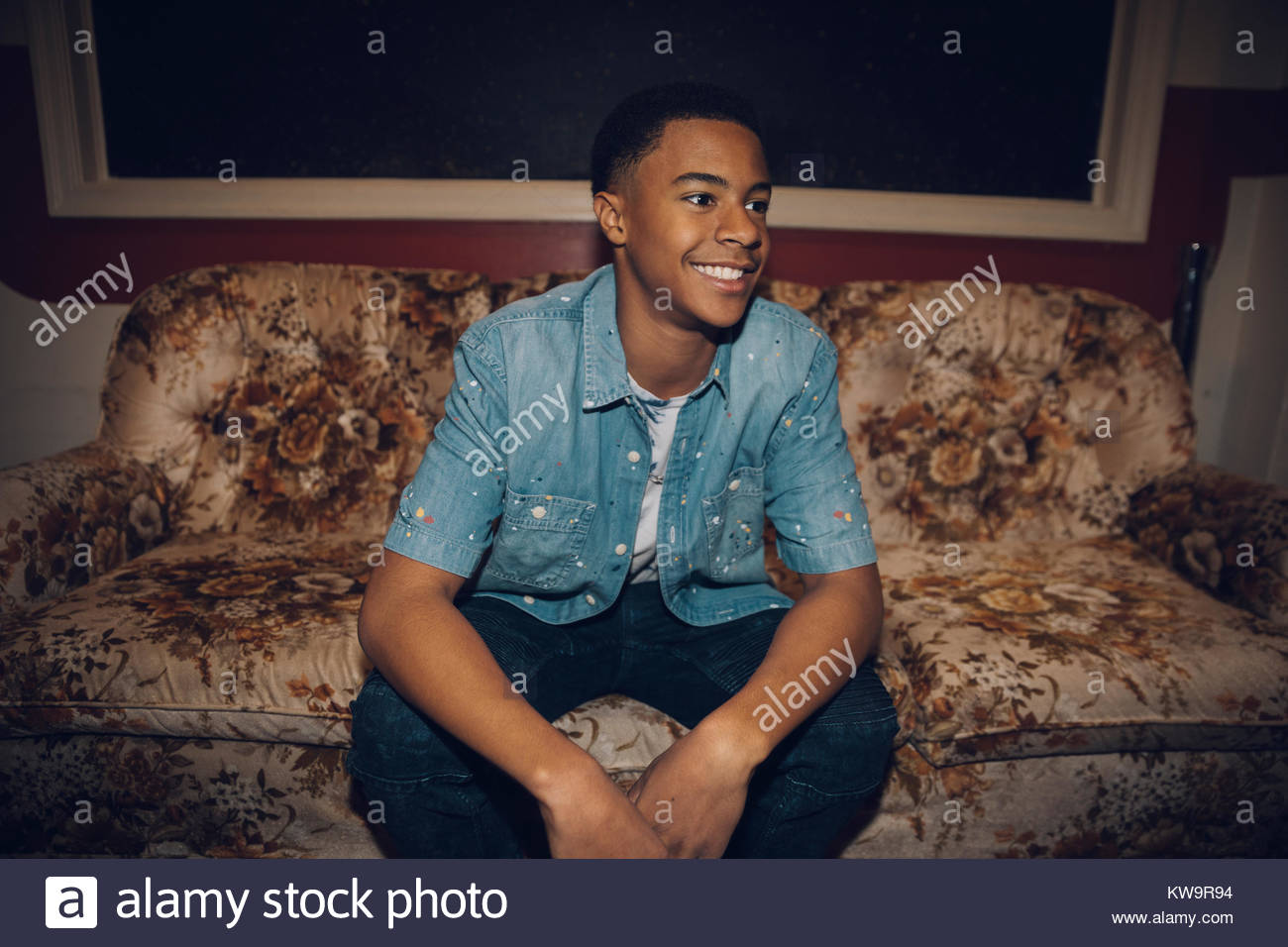 Sorridente,fiducioso African American tween ragazzo seduto sul divano,guardando lontano Foto Stock