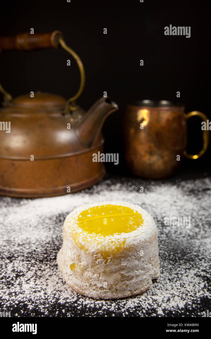 Torta al limone con zucchero a velo su sfondo scuro con rame antico tè pentola e mug Foto Stock