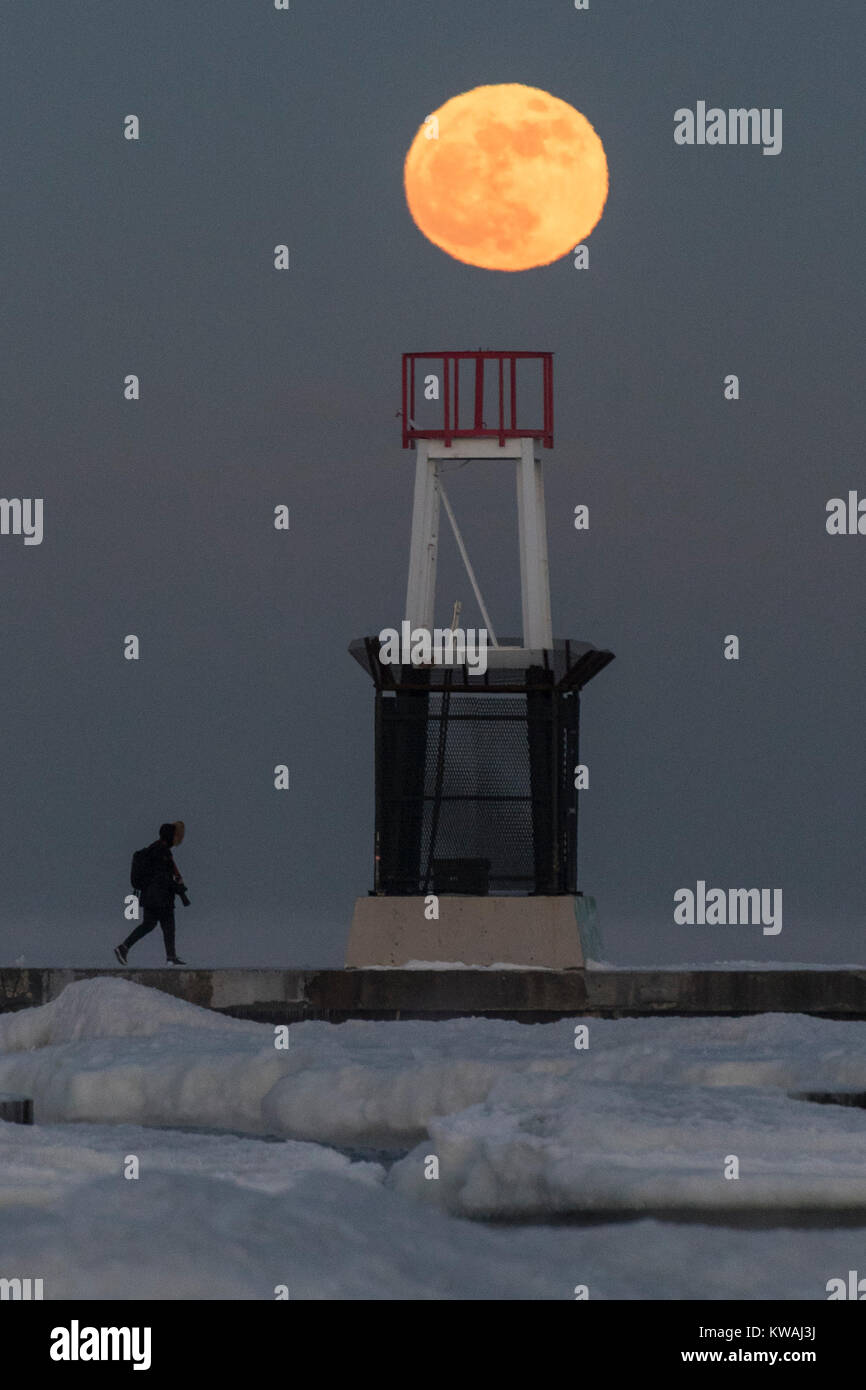 Chicago, Stati Uniti d'America. 1a gen, 2018. Un uomo cammina attraverso il molo al coperto di ghiaccio North Avenue beach come supermoon sorge su una delle più fredde Capodanno in decenni. La luna è al suo punto più vicino, il perigeo, a terra durante la sua orbita mensile e compare il 30% più luminoso e 14% più grande. Gennaio 2018 vede un supermoon noto come 'Wolf moon" il 1 gennaio e un "Blue Moon" il 31 gennaio. Credito: Stephen Chung/Alamy Live News Foto Stock