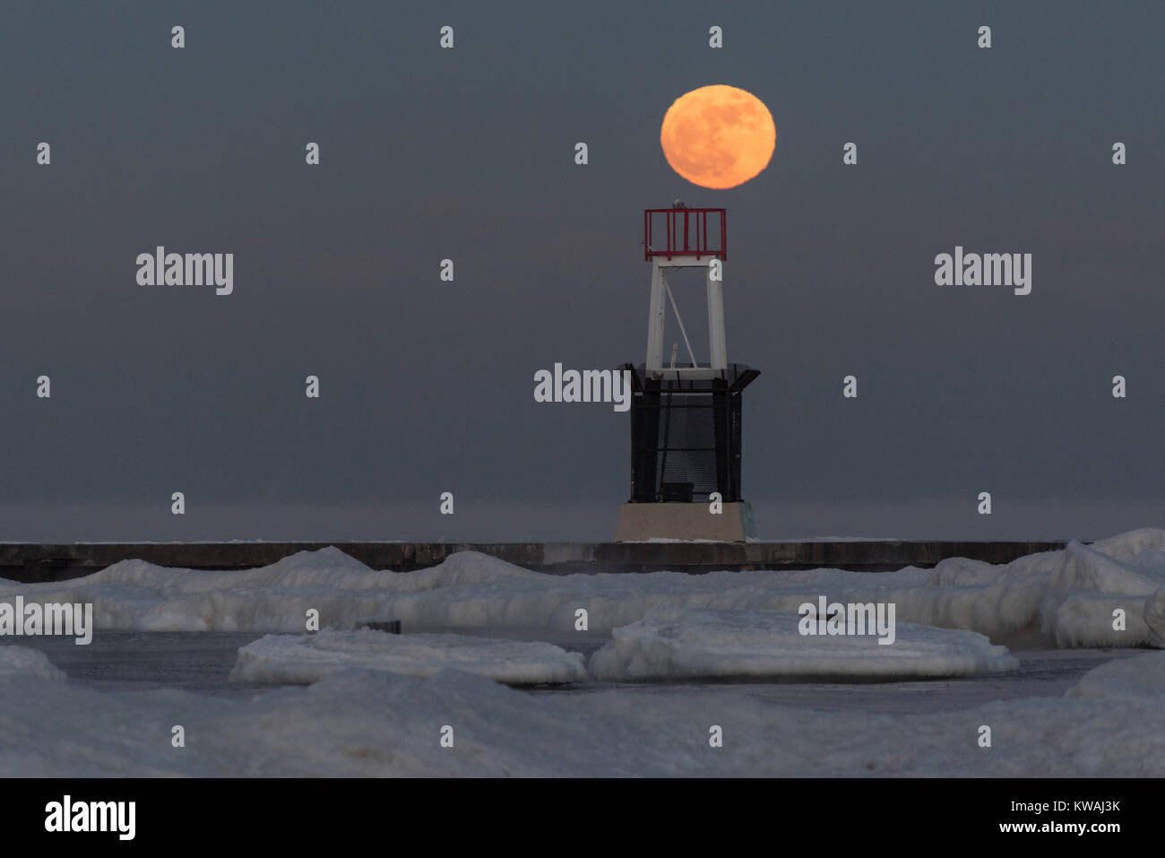 Chicago, Stati Uniti d'America. 1a gen, 2018. Una civetta delle nevi si siede in cima al faro a luce rotante sul molo al North Avenue beach come supermoon sorge su una delle più fredde il giorno di Capodanno in decenni. La luna è al suo punto più vicino, il perigeo, a terra durante la sua orbita mensile e compare il 30% più luminoso e 14% più grande. Gennaio 2018 vede un supermoon noto come 'Wolf moon" il 1 gennaio e un "Blue Moon" il 31 gennaio. Credito: Stephen Chung/Alamy Live News Foto Stock