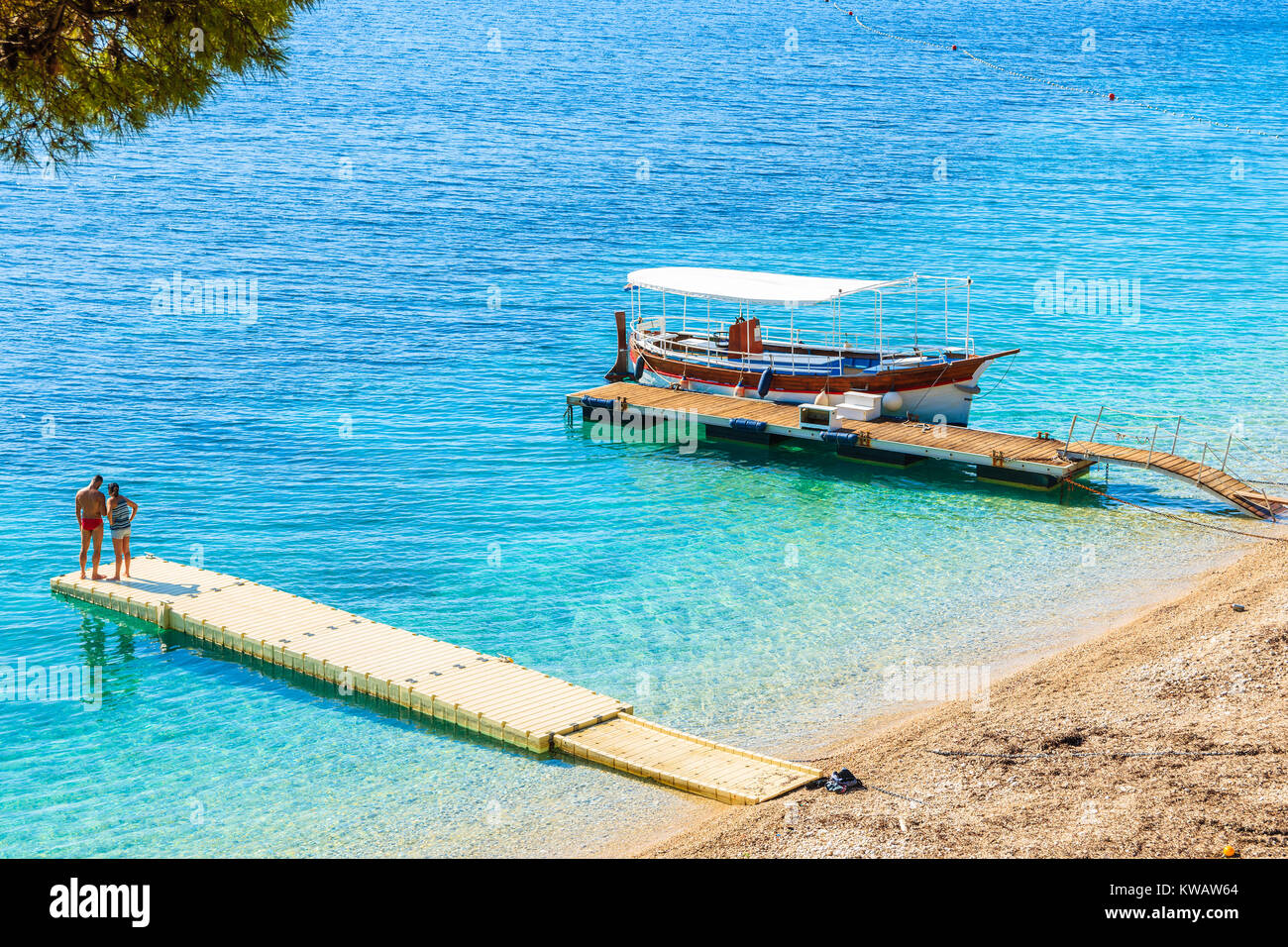 Unidentified giovane coppia di persone in piedi sul molo alla famosa spiaggia Zlatni Rat con mare bellissimo acqua nella città di Bol, isola di Brac, Croazia Foto Stock