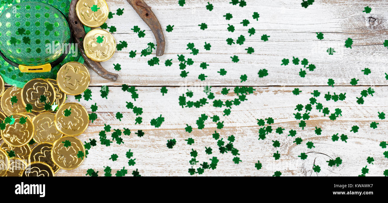 San Patrizio giorno buona fortuna hat, trifogli e a ferro di cavallo con oro lucido formando delle monete lungo il margine sinistro su bianco rustico di tavole di legno Foto Stock