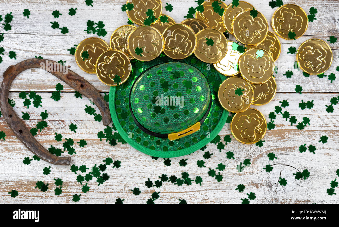 St Patrick buona fortuna hat, verde trifoglio e a ferro di cavallo con scintillante monete d oro su bianco rustico di tavole di legno Foto Stock