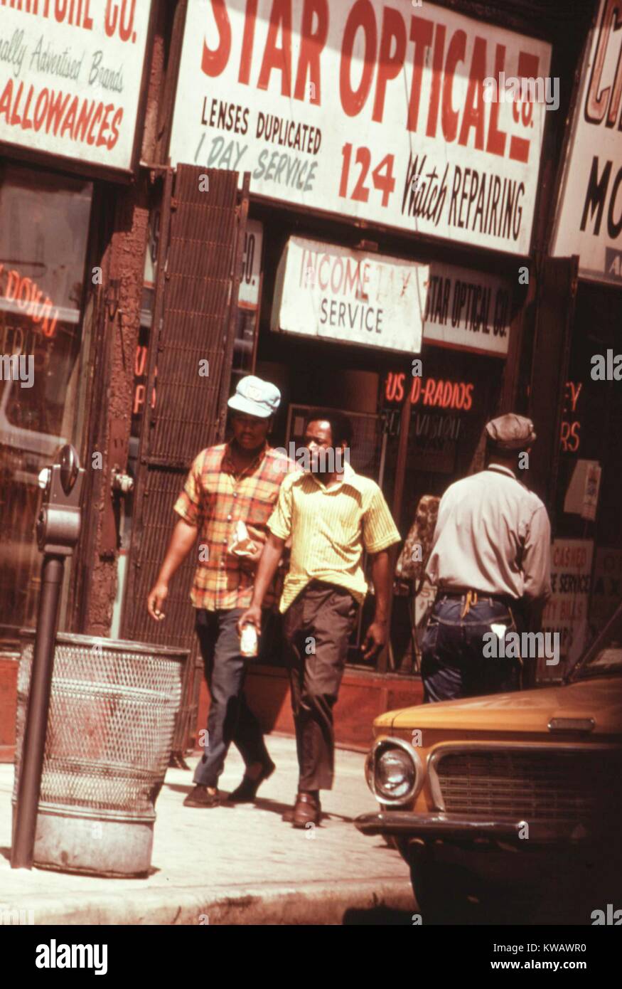 Due uomini camminare lungo un lato sud Chicago street foderato con edifici commerciali, Illinois, 1973. Immagine cortesia archivi nazionali. Foto Stock