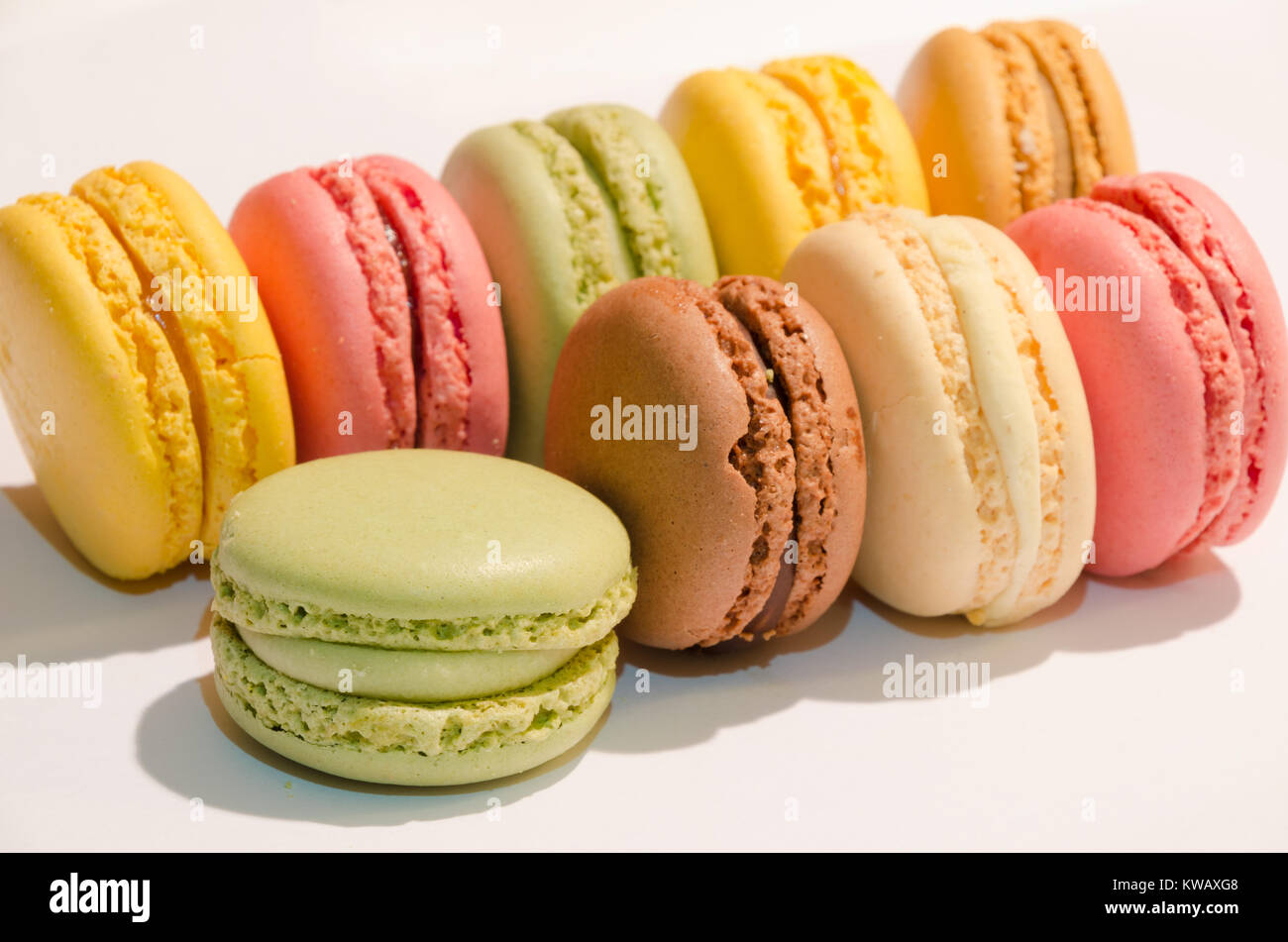 Nove macarons in diversi colori allineate su uno sfondo bianco Foto Stock