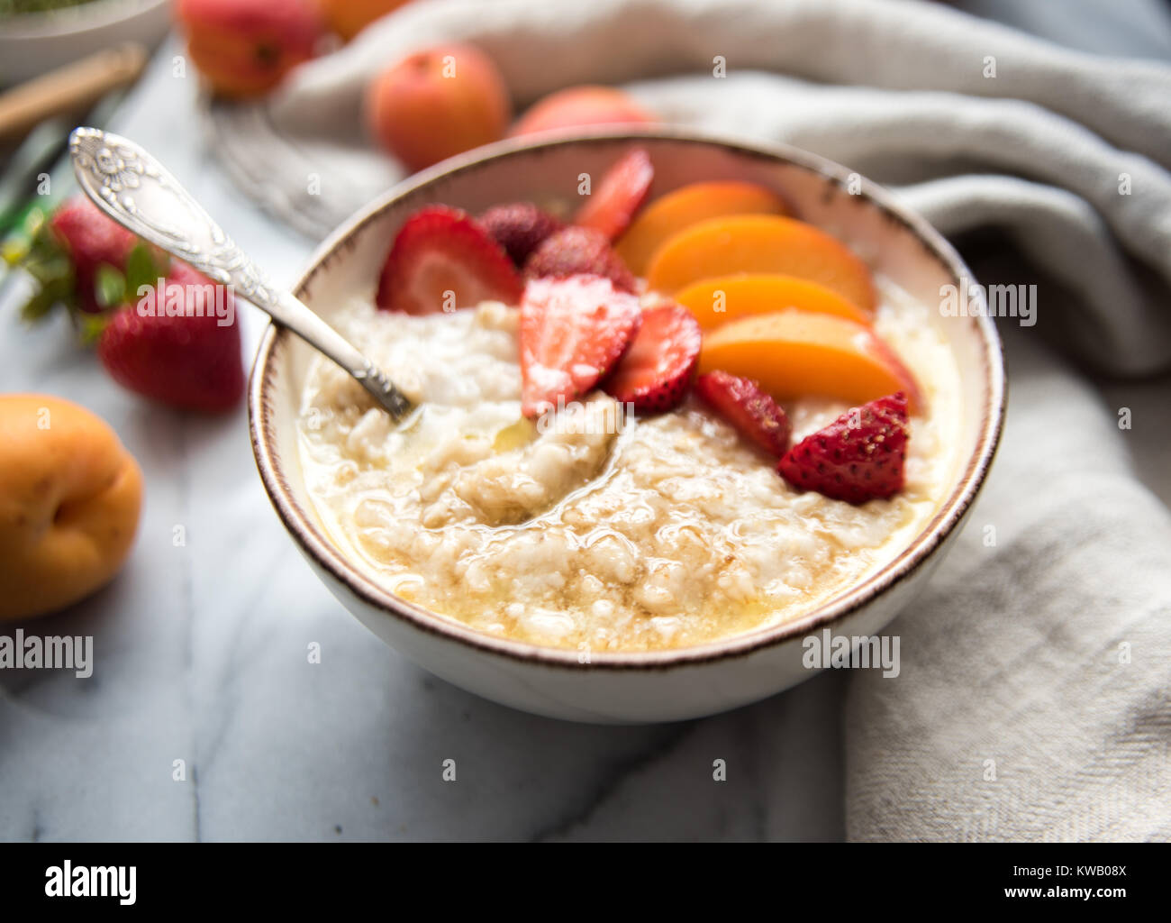 Calda tazza di cereali servita con prodotti freschi di pesche e di fragole per una sana prima colazione Foto Stock