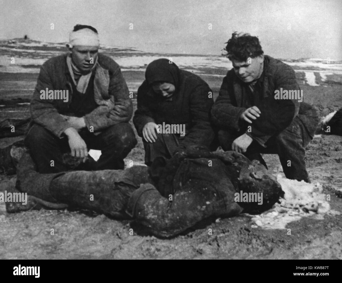 Conseguenze di un massacro tedesco dei soviet (russi) nella penisola di Kerch, Crimea. La famiglia Polyarush inginocchiati accanto al corpo del loro padre, 68-anno-vecchio Illarion. Nello stesso massacro, suo figlio primogenito Ivan (sinistra) è stato ferito in testa, ma si trovava ancora coperto di terra e di cadaveri. Di notte ha strisciato per un sicuro nascondiglio. Aprile 1942. Guerra mondiale 2. (BSLOC 2014 8 43) Foto Stock