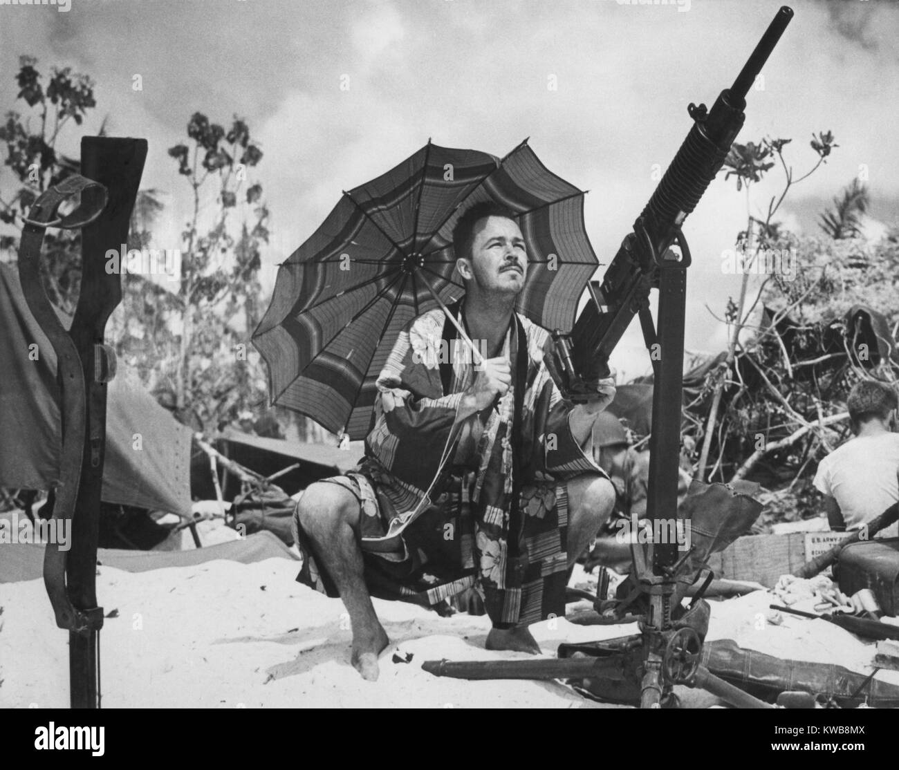 Stati Uniti Coast Guard invasore di Saipan è fuori di uniforme. Indossa un kimono di seta sotto l'ombra di un ombrellone pastello, egli prende la mira su un parrocchetto con un catturato Jap pistola. Ca. Giugno 1944. Isole Marianne Settentrionali, guerra mondiale 2. (BSLOC 2014 10 107) Foto Stock