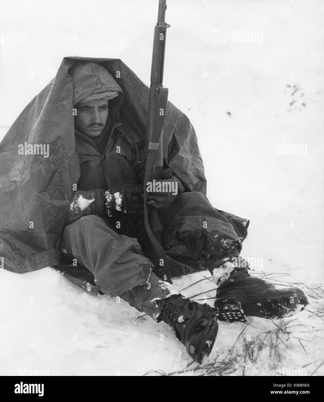Soldato dell'U.S. Xix Reggimento di Fanteria usa il suo poncho di ottenere protezione dal vento pungente e freddo. Area Yoju gen. 10, 1951, dopo il ritiro delle forze ONU dalla Corea del Nord. Guerra di Corea, 1950-1953. (BSLOC 2014 11 71) Foto Stock