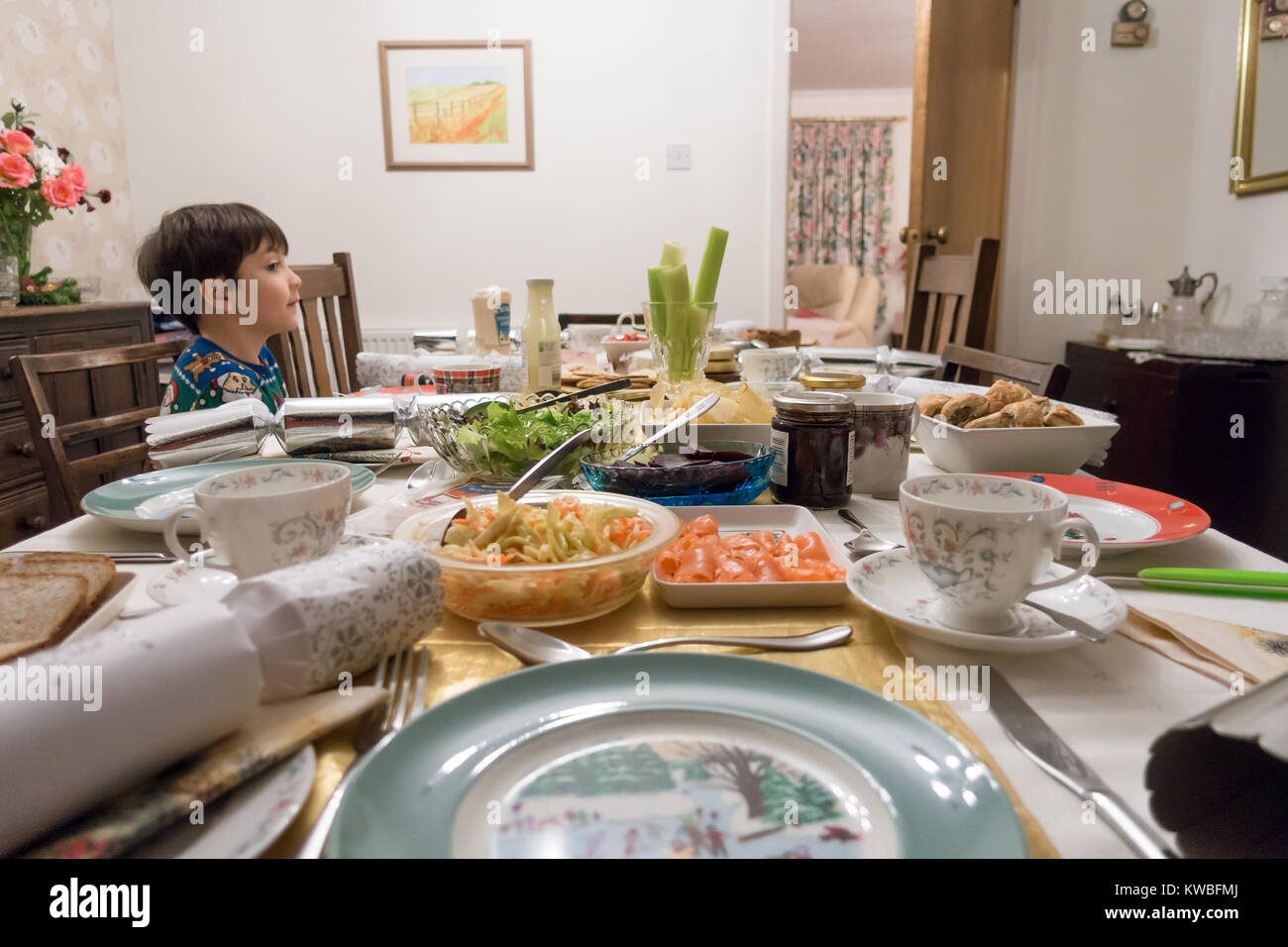 Un ragazzo si siede e attende palesemente al tavolo da pranzo per il resto della sua famiglia ad unirsi a lui per mangiare tè di Natale costituito da insalata. Foto Stock
