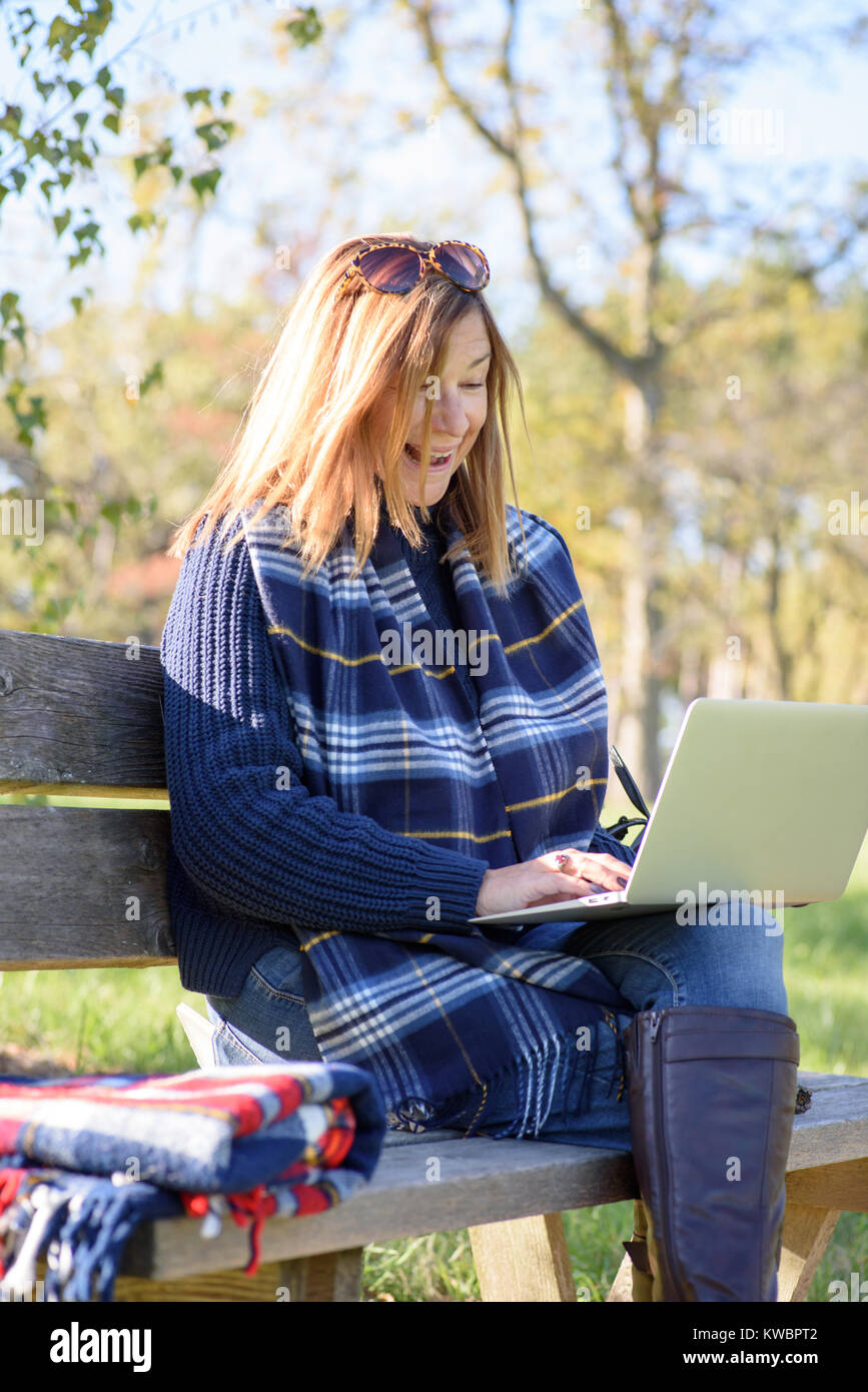 Donna al lavoro su computer portatile esterno su una panchina nel parco sulla soleggiata giornata di caduta Foto Stock