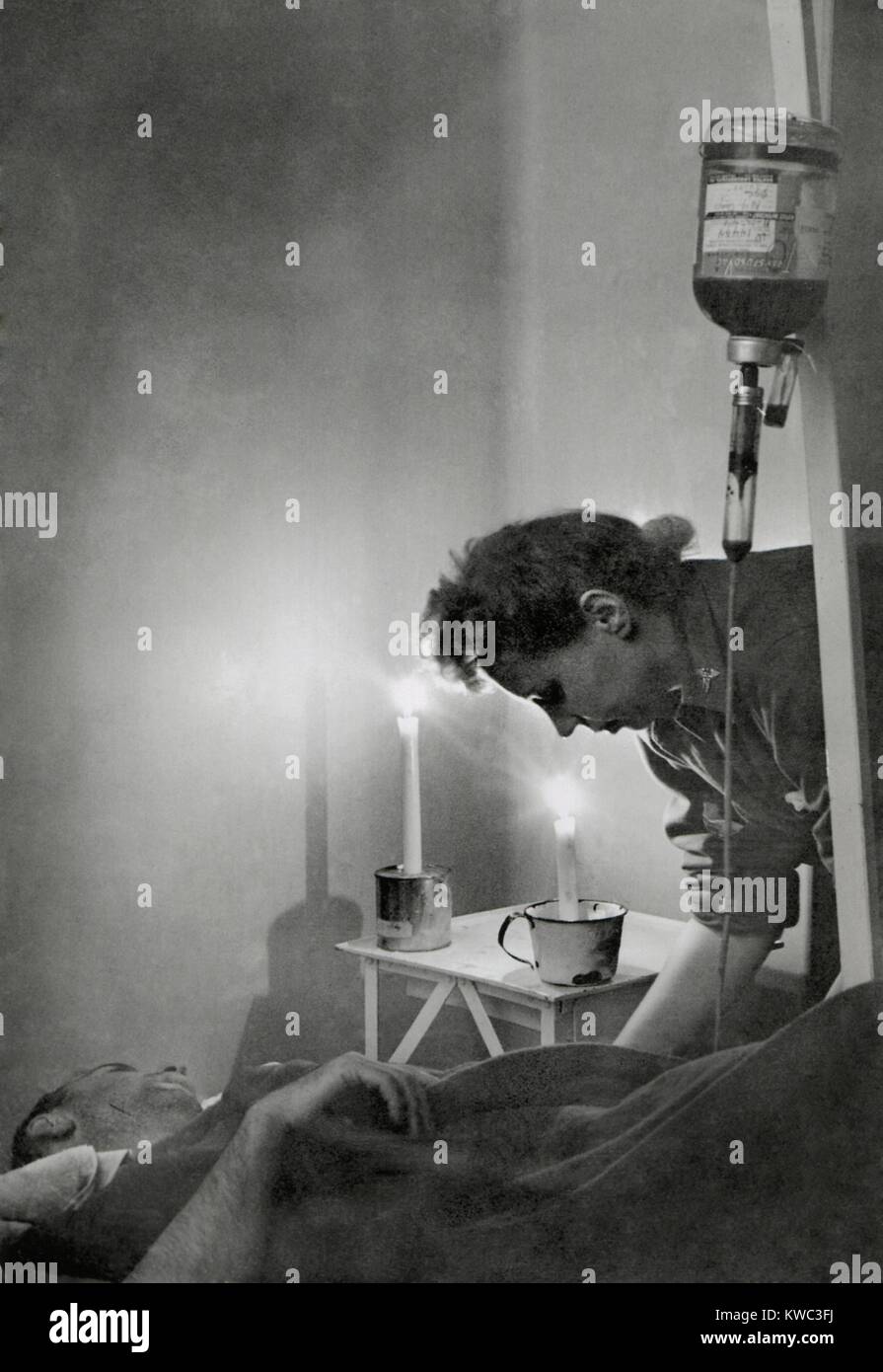 Esercito Americano infermiera della candela accesa posto letto del soldato ferito in Francia durante la Prima Guerra Mondiale 2. Egli riceve una trasfusione in corrispondenza di una linea di fronte ospedale indicando una grande perdita di sangue dalla sua ferita. Jan 23, 1945. (BSLOC 2015 13 83) Foto Stock