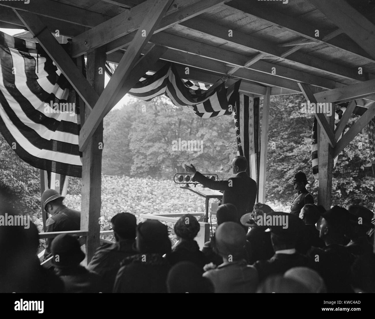 Presidente Calvin Coolidge parlando a una folla all'aperto. Egli parla di un bunting decorate enclosure con microfoni in 1928. (BSLOC 2015 15 148) Foto Stock