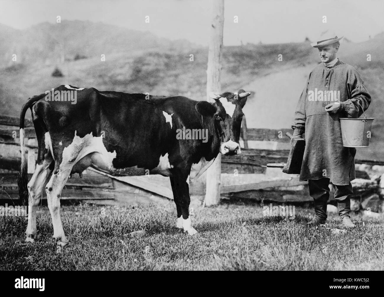 Calvin Coolidge indossando un camiciotto e stivali in pelle, si avvicina ad una vacca da latte. Il presidente futuro portato un secchio e la mungitura sgabello sul suo padre nella fattoria di Plymouth, Vermont. Ca. 1920-23. (BSLOC 2015 15 158) Foto Stock