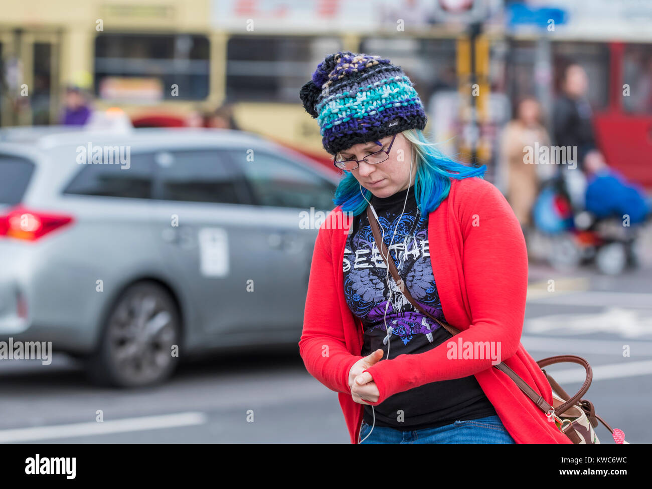 Giovane donna casual da indossare abbigliamento invernale e un berretto lavorato a maglia a piedi con la sua testa in basso in una città nel Regno Unito. Foto Stock