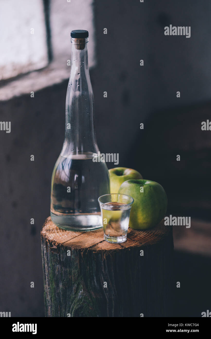 Apple brandy, rustica atmosfera rétro. Bottiglia e unico colpo di vetro con alcool bere e due verde mela frutta. Foto Stock