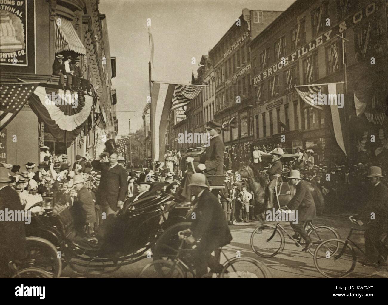 Theodore Roosevelt in piedi in un carrello, il ribaltamento il suo cappello, scortati dalla polizia di biciclette nel 1902. Posizione non identificato (BSLOC 2017 4 54) Foto Stock
