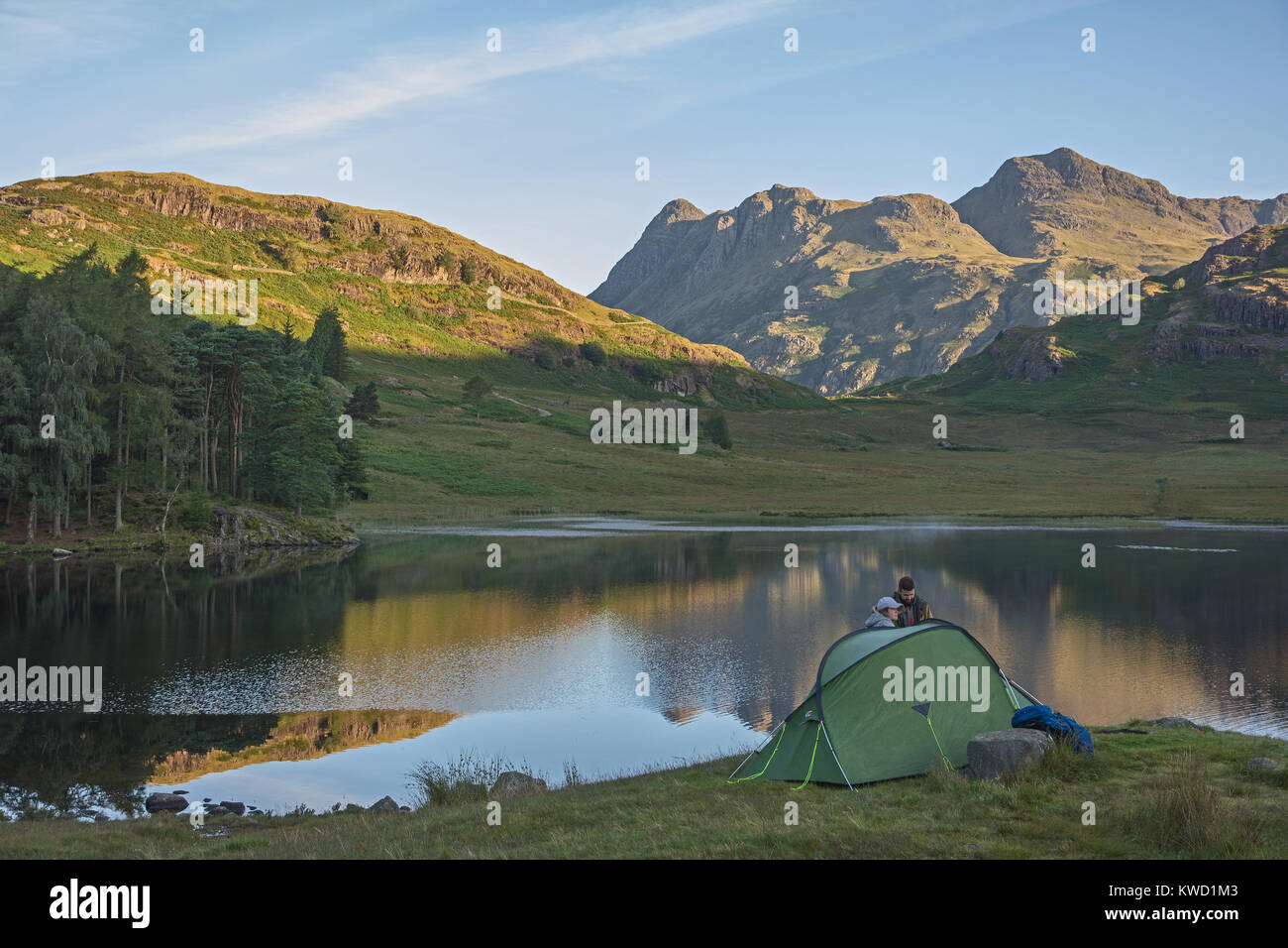 Blea Tarn e The Langdale Pikes Cumbria Lake District inglese in Inghilterra su mattinata estiva con sole splendente e riflessioni con tenda e camper due Foto Stock