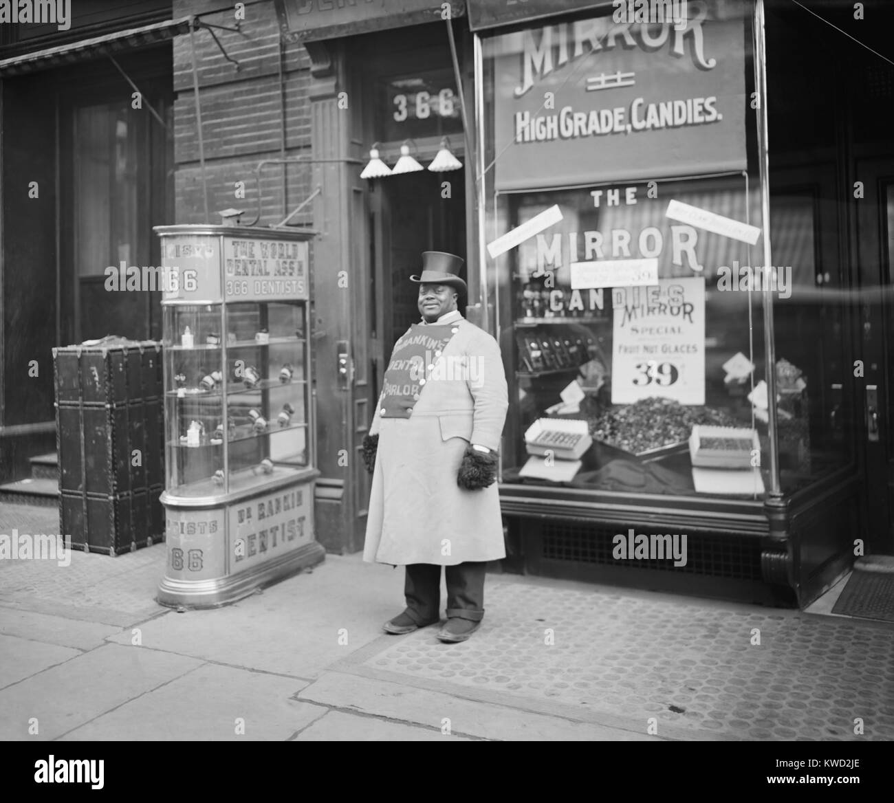African American promuovere il dottor Ranklins dentale con salotto sul suo petto raddoppiato cappotto. La porta di 366 Fifth Avenue in aperta e un caso di vetro Visualizza set di denti finti. La città di New York, 1900-1910. (BSLOC 2017 20 95) Foto Stock