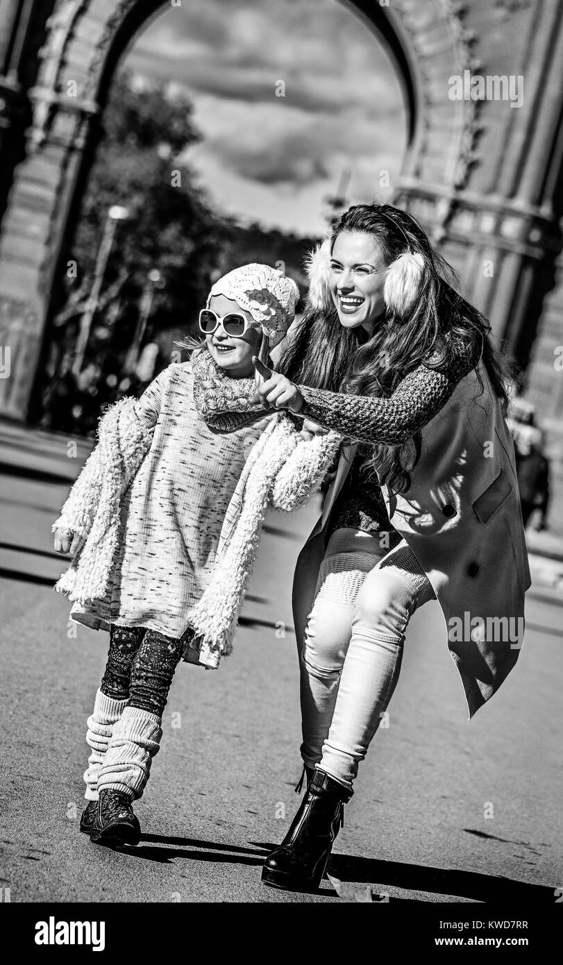 A Barcellona per una perfetta inverno. A piena lunghezza Ritratto di felice madre alla moda puntando su qualcosa di bambino vicino al Arc de Triomf a Barcellona, Spagna Foto Stock