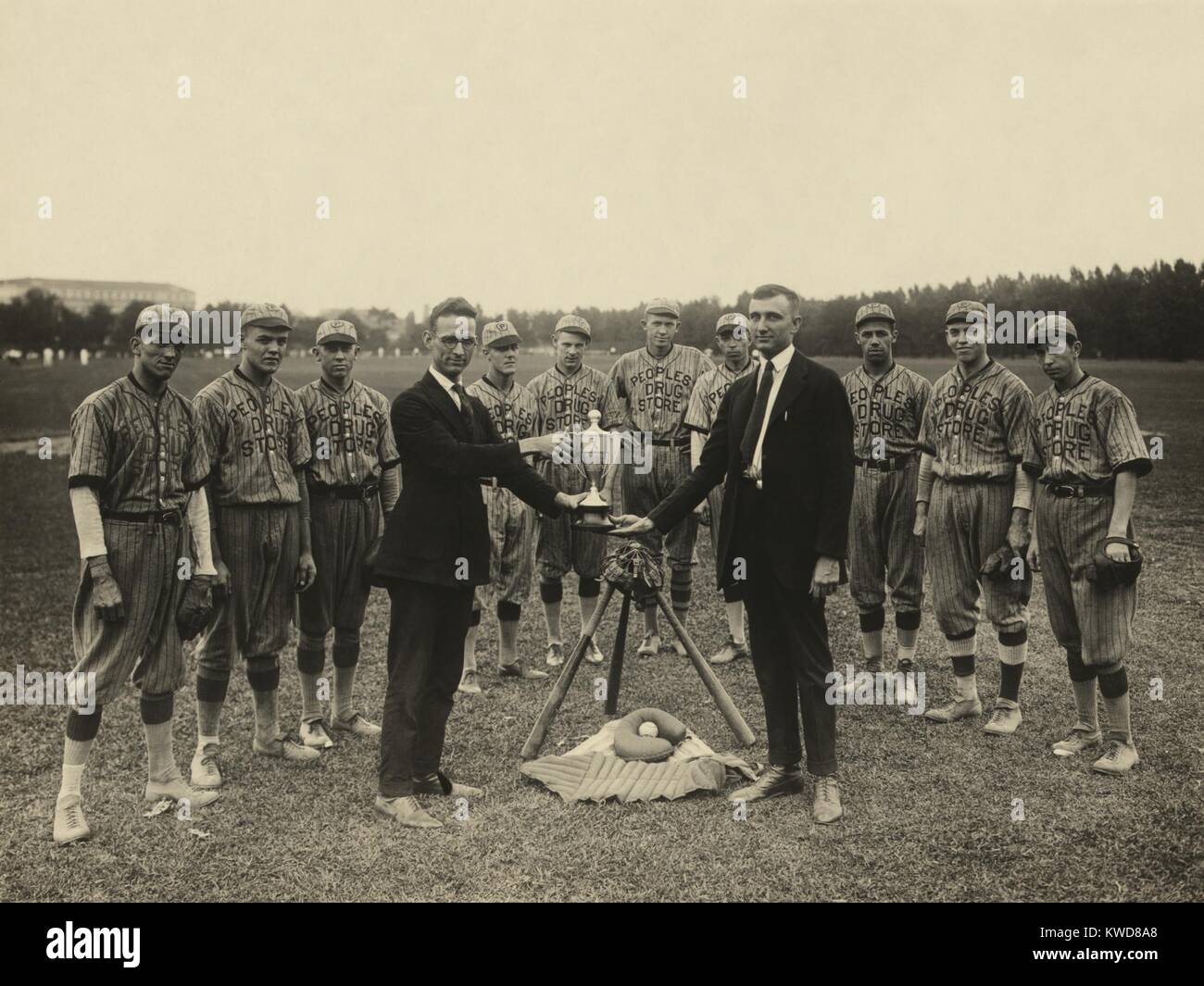 Persone di Drug Store squadra di baseball pongono permanente con il loro trofeo, 1921. Il Washington, D.C. squadre amatoriali che sta dietro un simbolico tableau di attrezzatura da baseball come due uomini in abiti exchange il trofeo. (BSLOC 2015 17 2) Foto Stock