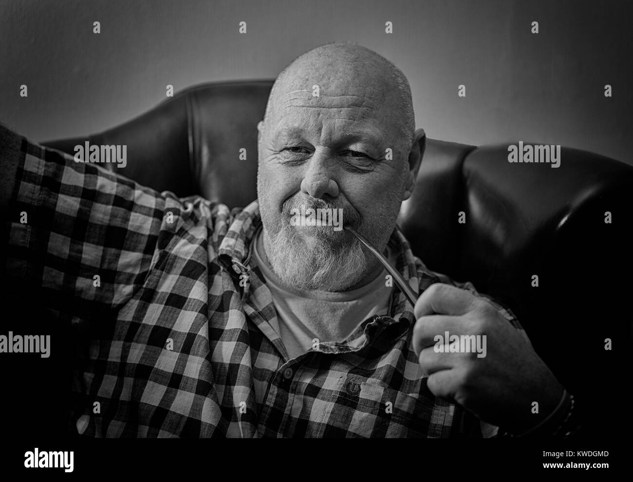 Un maschio maturo seduto in una poltrona tenendo una tubazione in un umore riflettente. Foto Stock