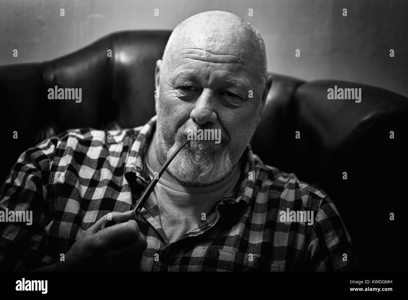 Un maschio maturo seduto in una poltrona tenendo una tubazione in un umore riflettente. Foto Stock