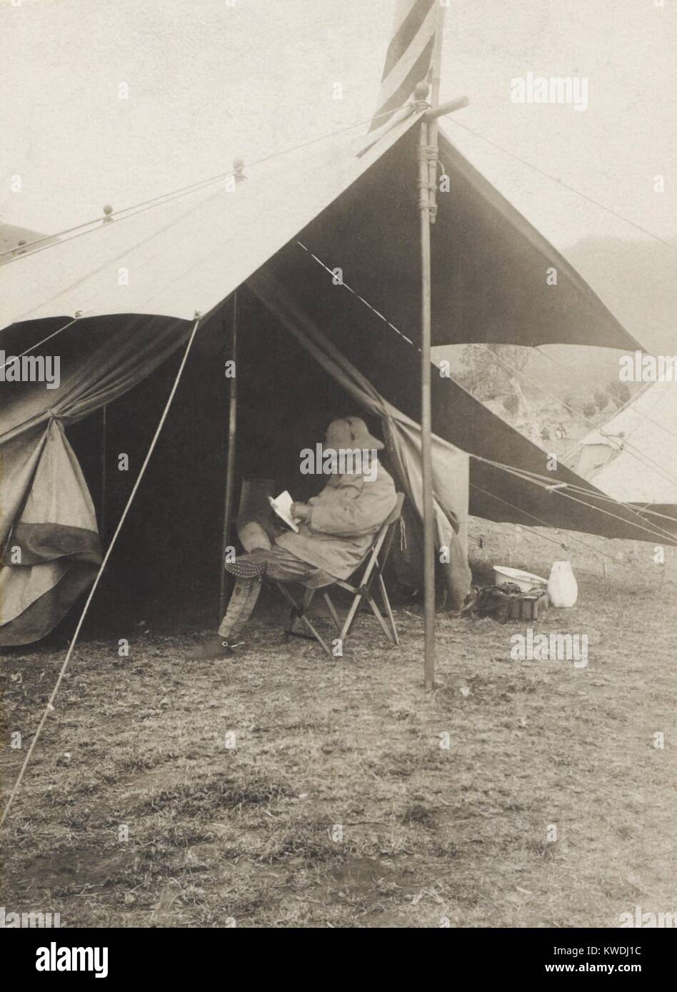 Theodore Roosevelt la lettura di fronte la sua tenda nella caccia camp, 3-4 giugno, 1909. Kijabe, British East Africa (Kenya) durante lo Smithsonian-Roosevelt spedizione africana (BSLOC_2017_8_5) Foto Stock