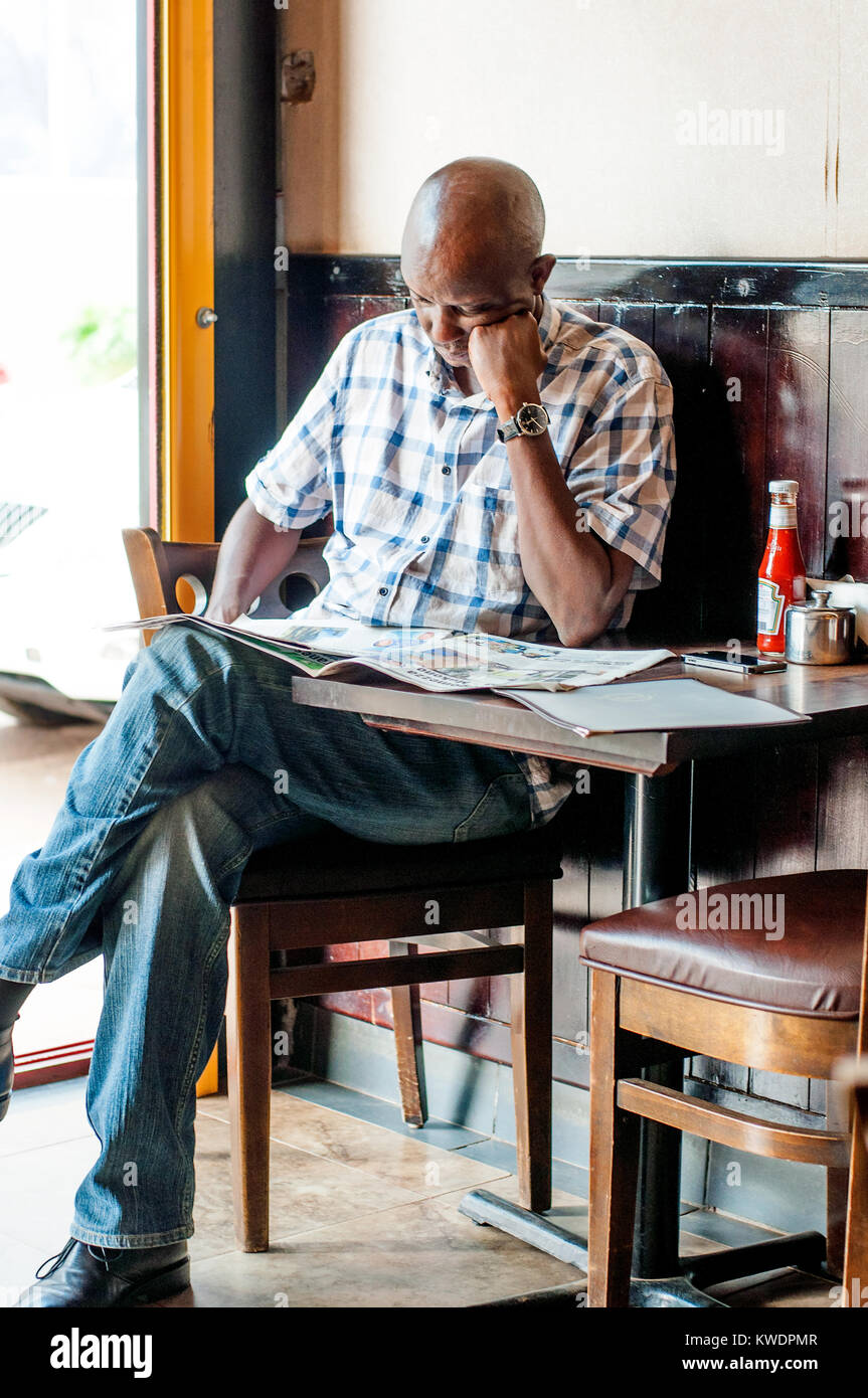 Manb leggendo il giornale in coffee shop, Kampala, Uganda Foto Stock