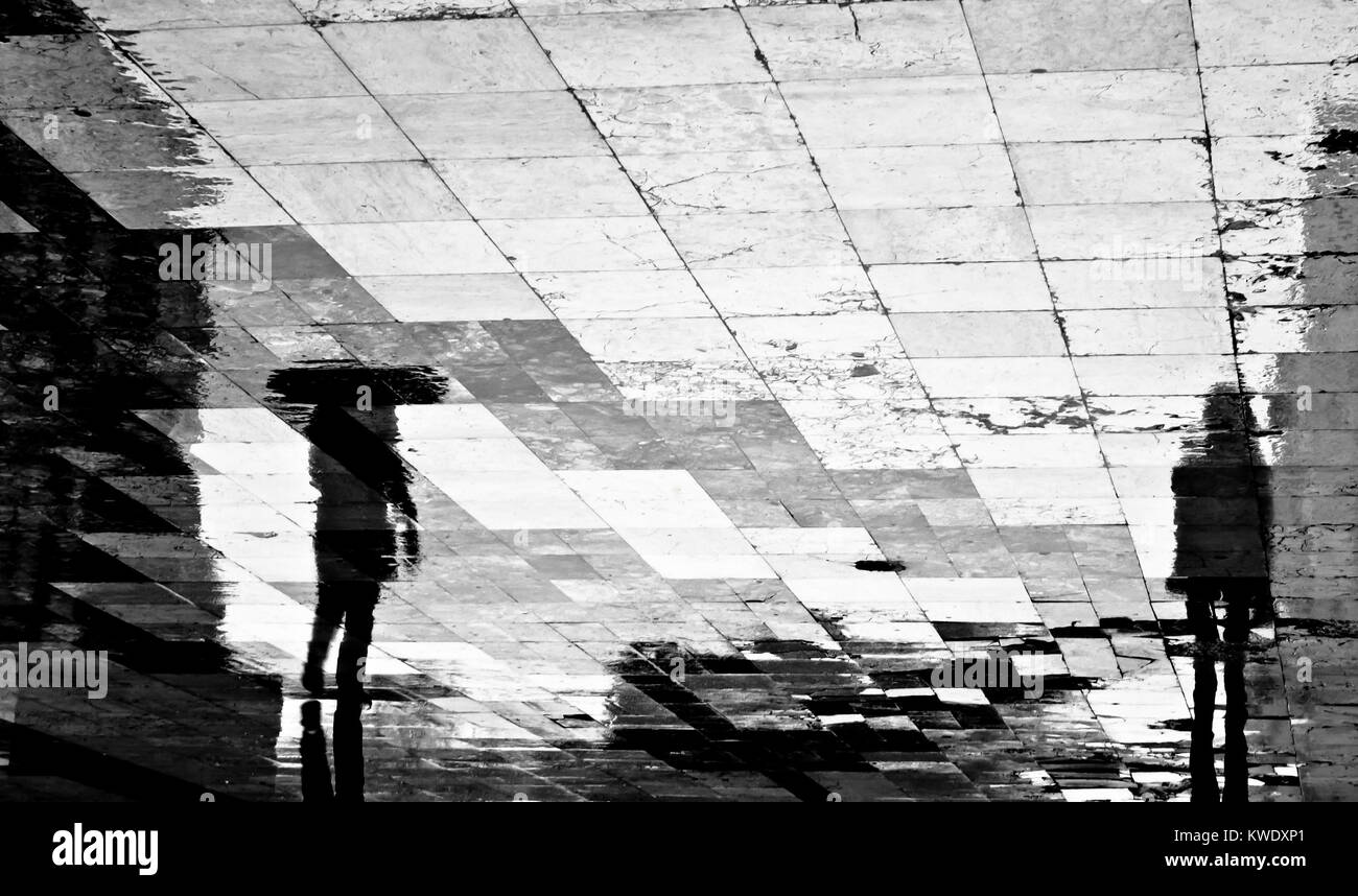 Sfocata riflessione ombra silhouette di due persone che camminano nella strada di città sotto la pioggia in bianco e nero Foto Stock