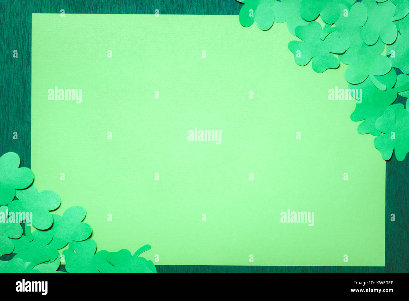 St Patrick concetto banner con molti trifogli di carta in due angoli opposti di una carta vergine, centrato su un verde scuro dello sfondo di legno. Foto Stock