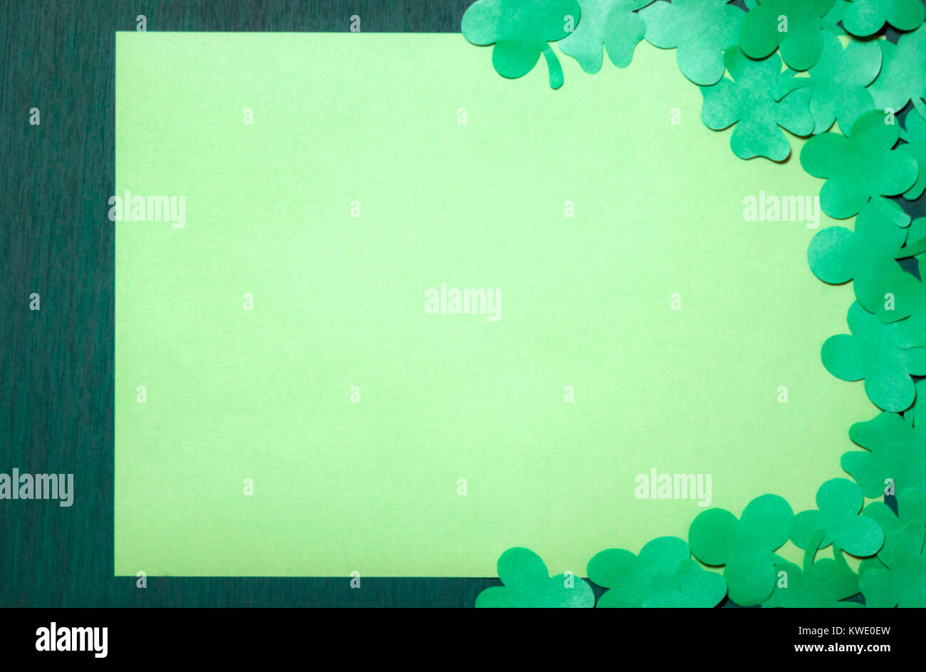 Saint Patrick greeting card design con un sacco di carta trifogli che circonda un giallo vuota del foglio di carta visualizzato su un verde scuro dello sfondo di legno. Foto Stock