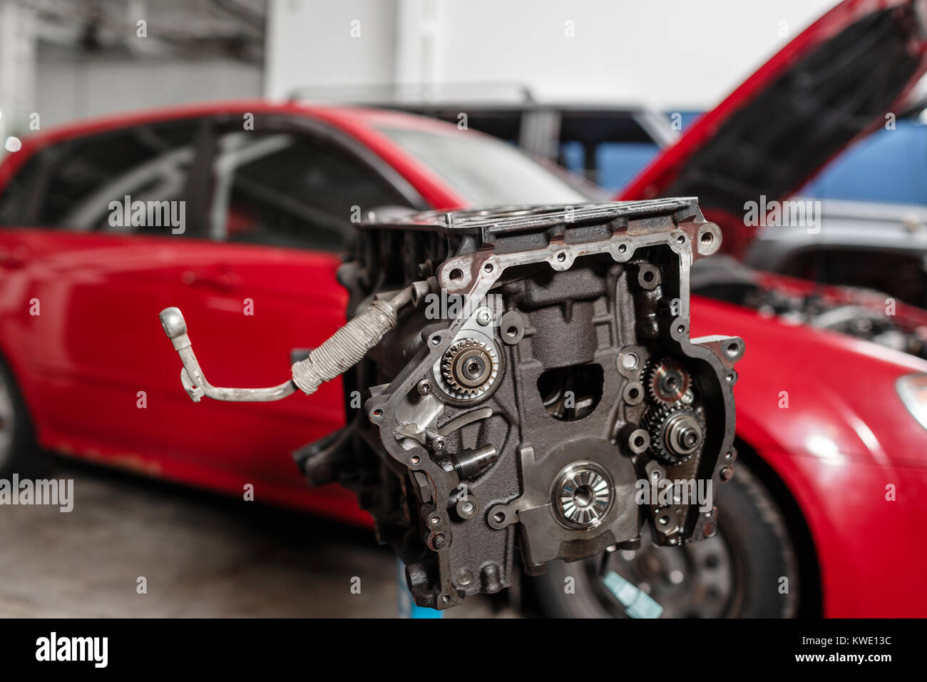 Messa a fuoco selettiva. Blocco del motore sul cavalletto di riparazione con il pistone e la biella di tecnologia automobilistica. Sfocato auto rossa sullo sfondo. Interno di una riparazione auto shop. Foto Stock