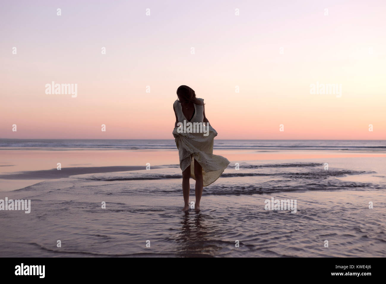 Donna abito di contenimento mentre si sta in piedi sul litorale di spiaggia contro il cielo chiaro durante il tramonto Foto Stock