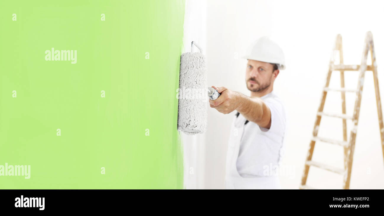 Pittore uomo al lavoro con un rullo di vernice, muro dipinto di colore verde concetto ecologico, web modello di pagina di intestazione Foto Stock