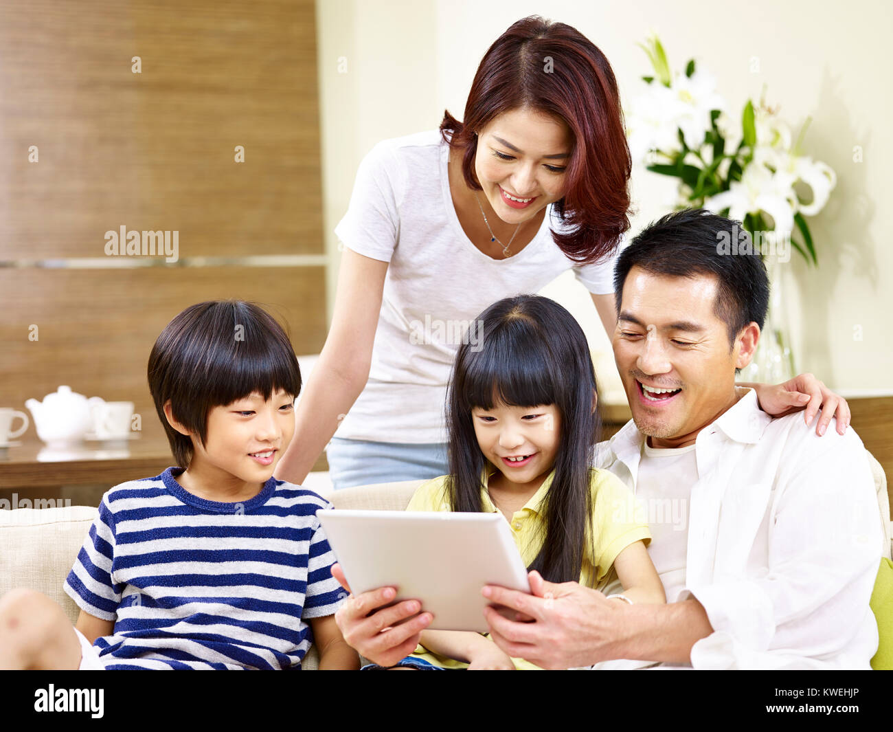 Asian genitori la madre e il padre e i due figli del figlio e figlia seduti sulla famiglia del lettino con tavoletta digitale insieme. Foto Stock