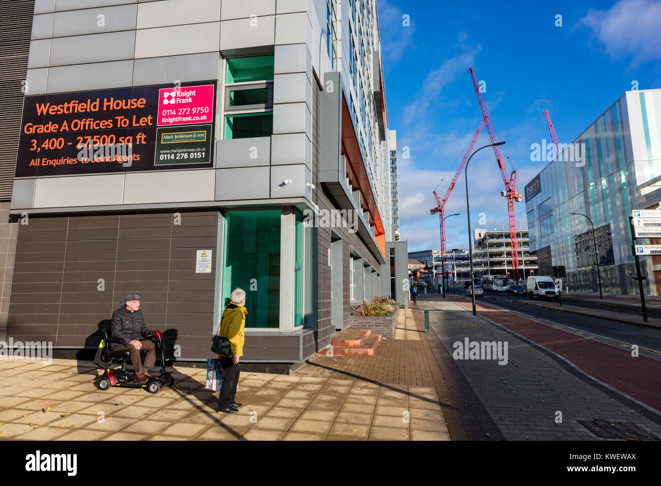 Una coppia di anziani, l'uomo in una sedia a rotelle riparo dal vento freddo nel centro della città di Sheffield in un freddo ma soleggiato inverni giorno, South Yorkshire, Regno Unito Foto Stock